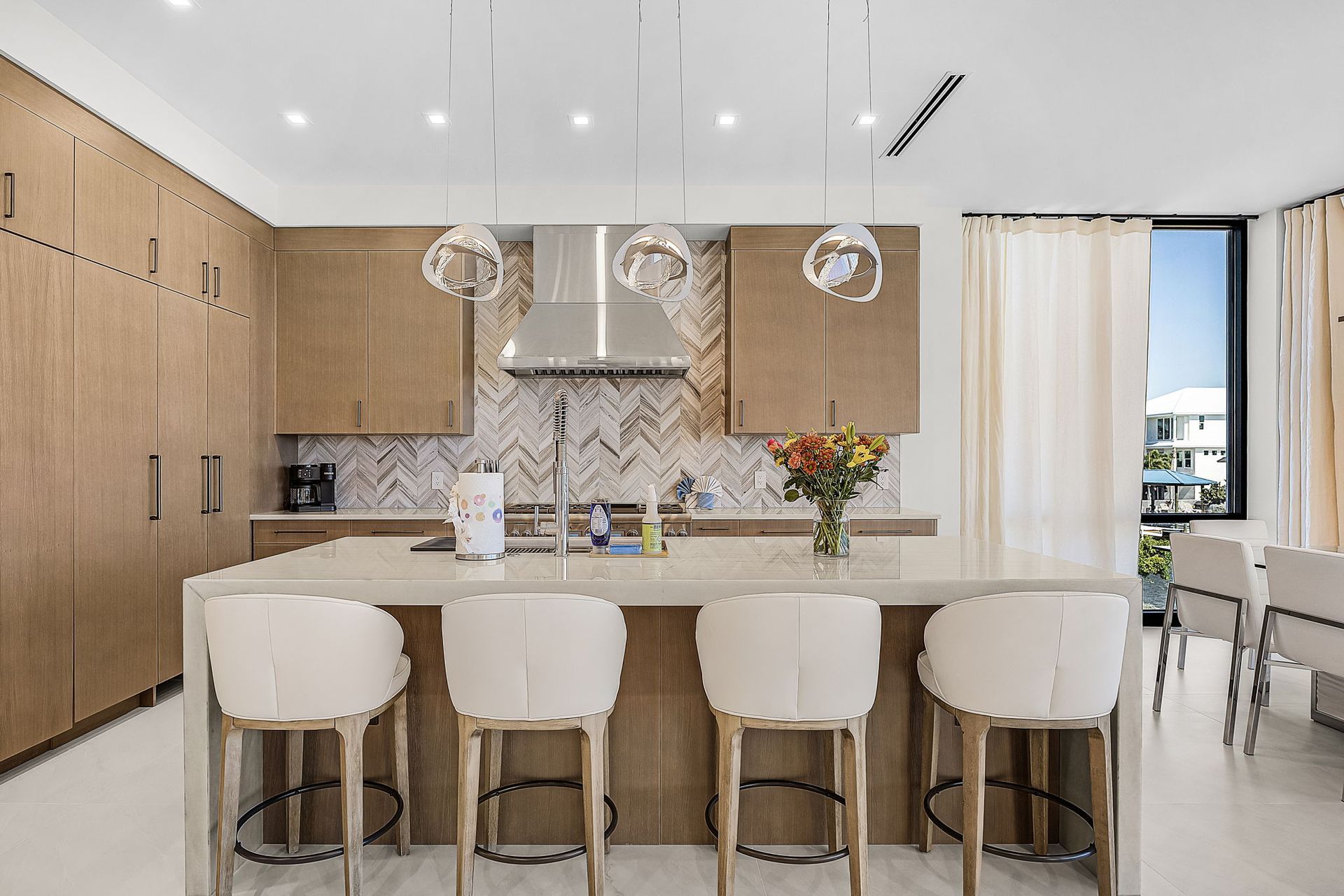 Modern kitchen with light wood cabinets, marble island, pendant lights, and bar stools.
