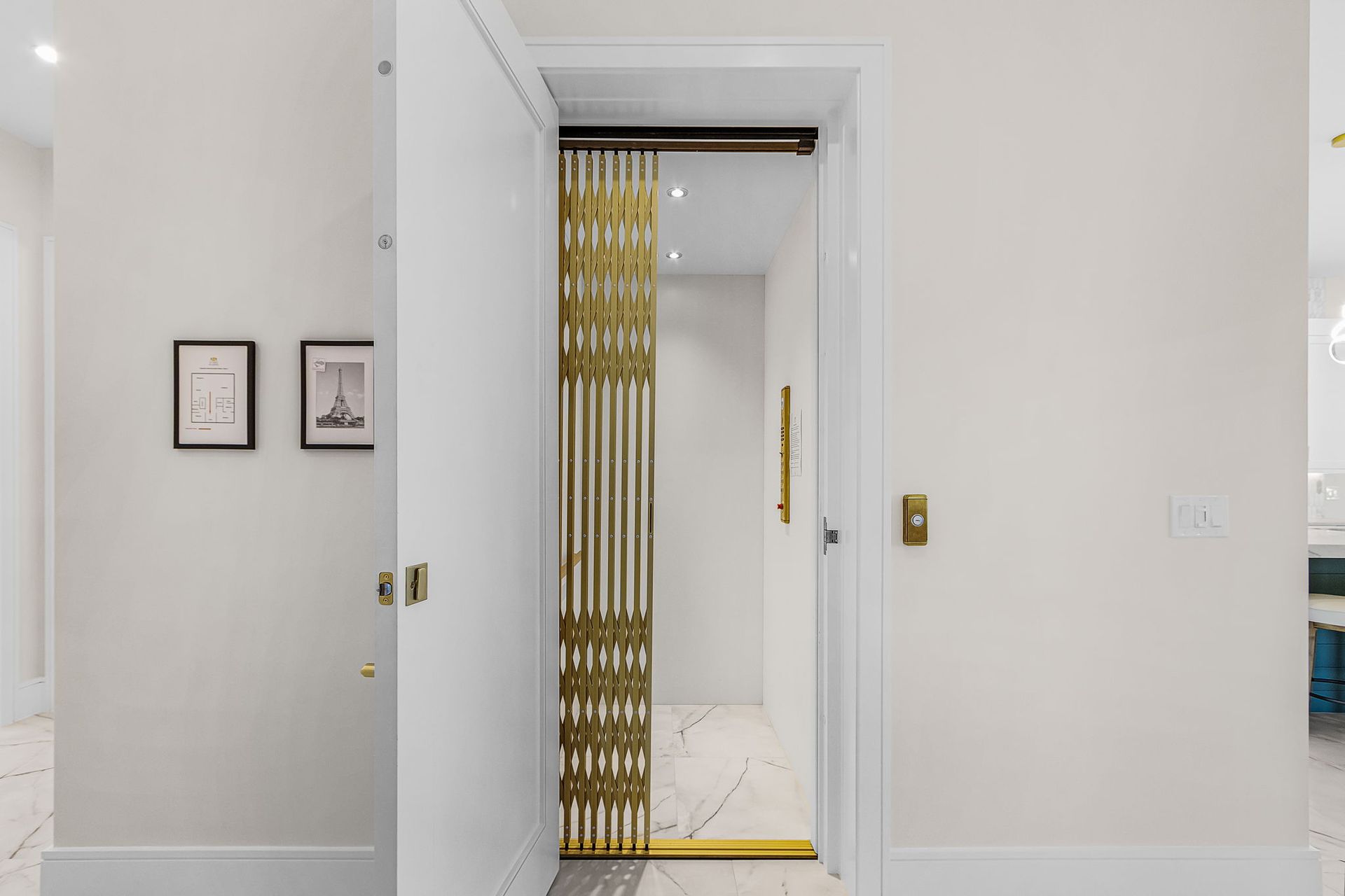 Open white door revealing an elevator with gold metal gate, white walls, and marble flooring.