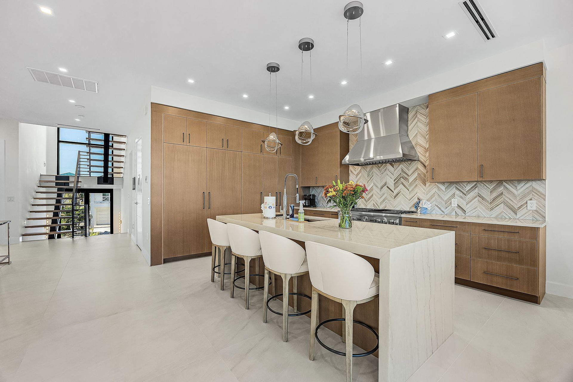 Modern kitchen with wood cabinets, island with stools, and staircase in the background.
