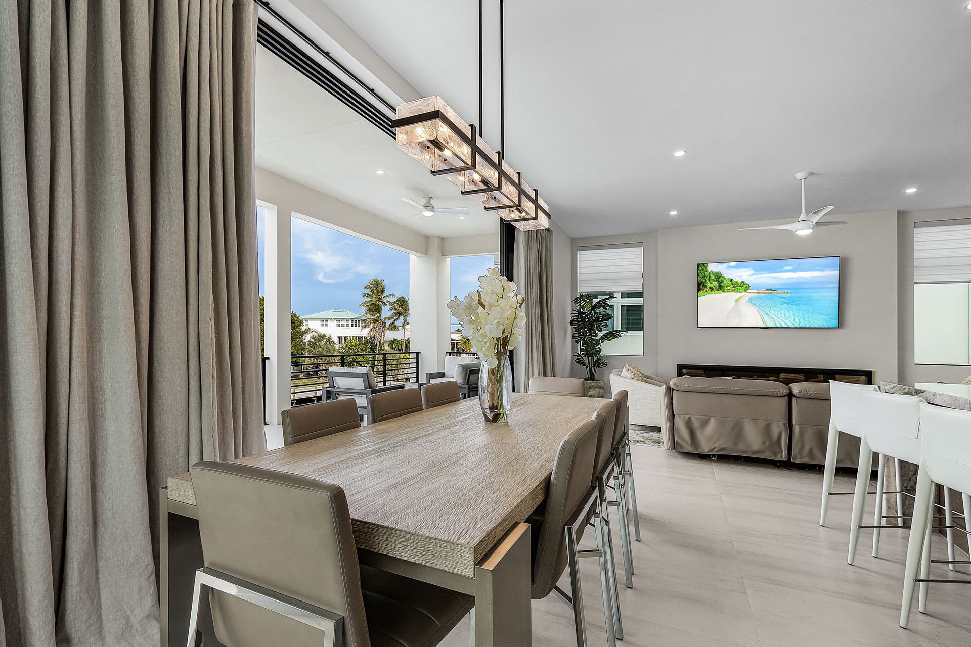 Dining room with long table and chairs, adjacent to an outdoor patio with ocean views.
