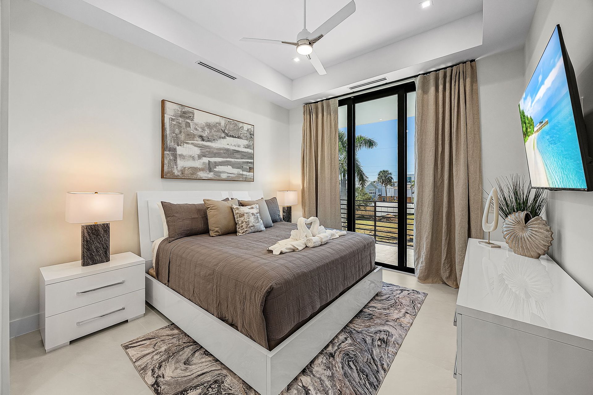 Bedroom with a king-size bed, white furniture, a large TV, and a sliding glass door to a patio.