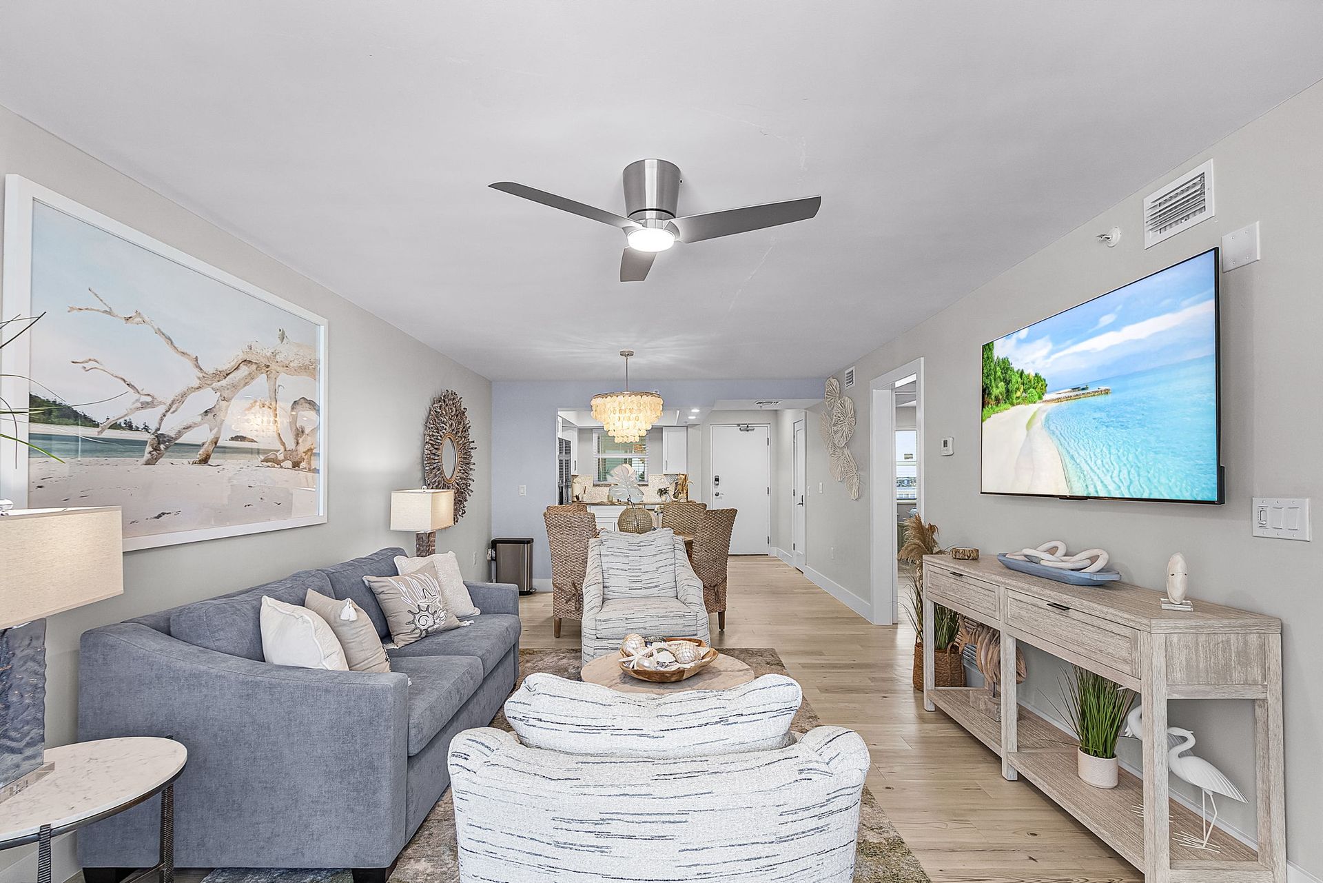 Living room with coastal decor, including a blue sofa, white armchair, and beach-themed artwork.