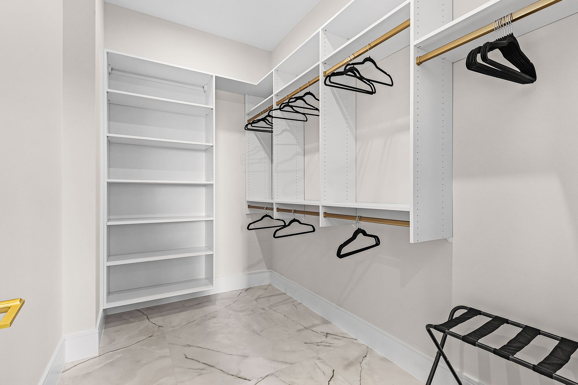 Empty walk-in closet with white shelves, hanging rods, and black hangers, gold accents.
