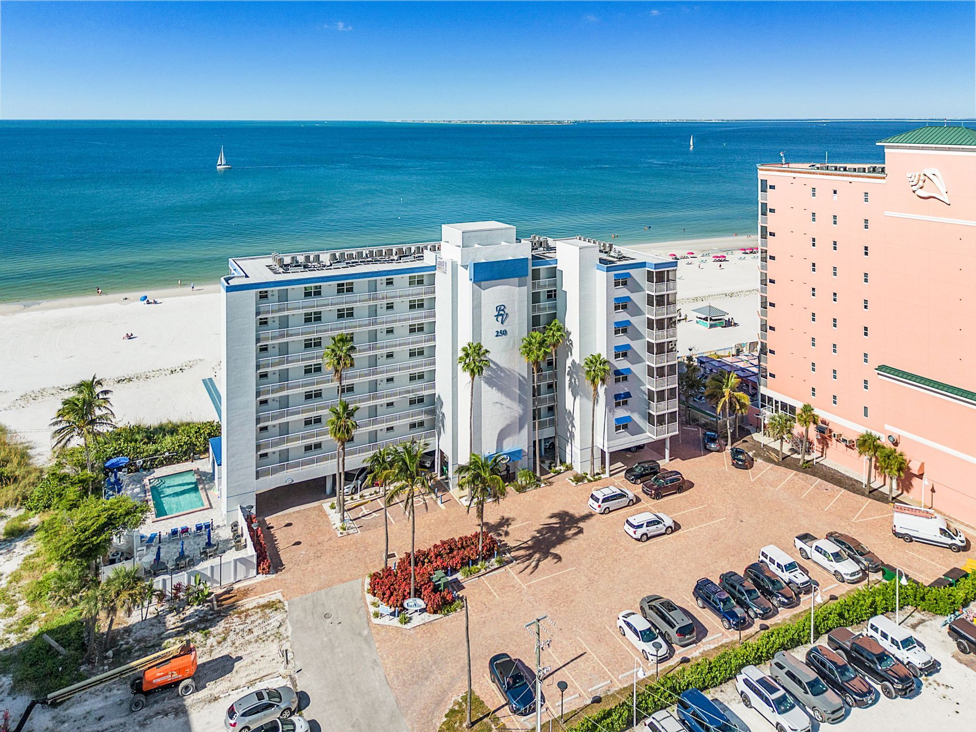 Beachfront hotel with a blue and white facade, cars in a parking lot, and the ocean in the background.