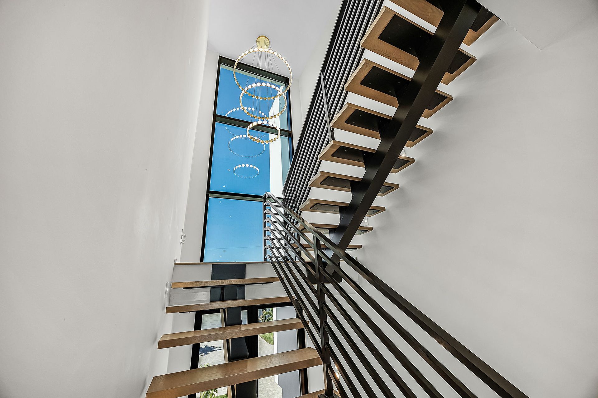 Staircase with wooden steps and black metal railing, next to a large window with a blue sky view.