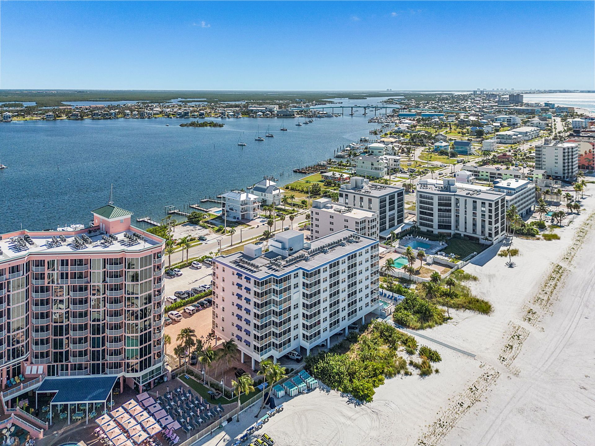 Aerial view of a coastal city with high-rise buildings, beach, and water under a blue sky.
