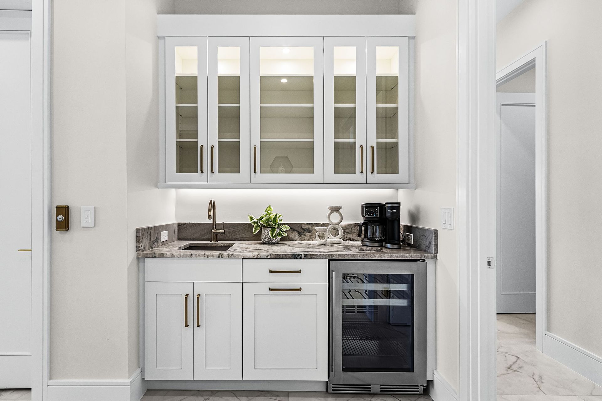 White wet bar with upper glass cabinets, a sink, and a wine fridge.