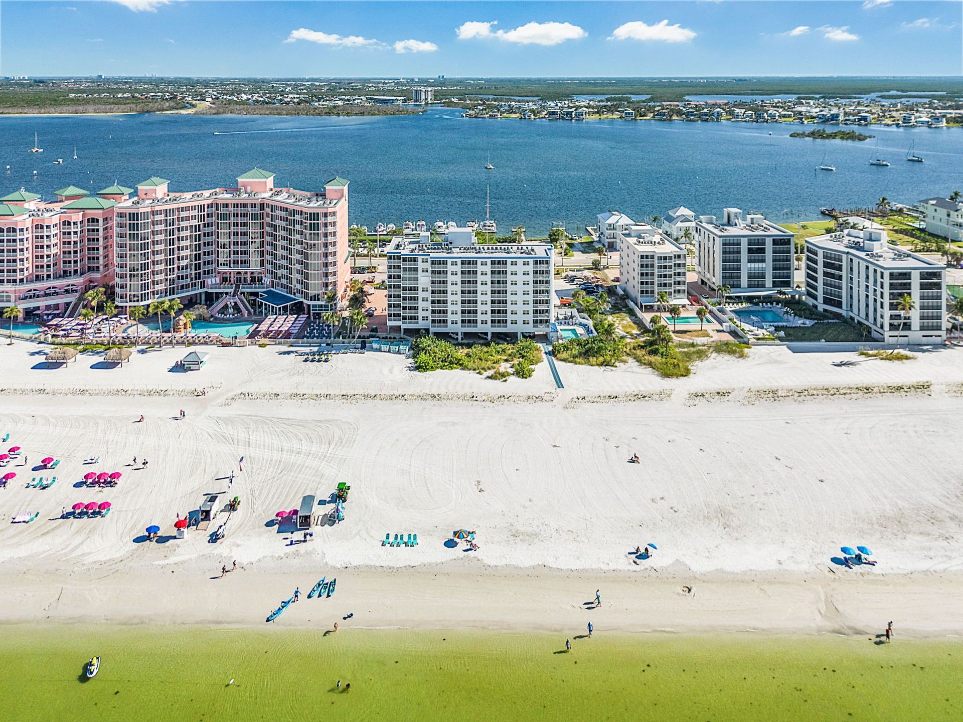 Beachfront view with buildings, ocean, and people on the sand.