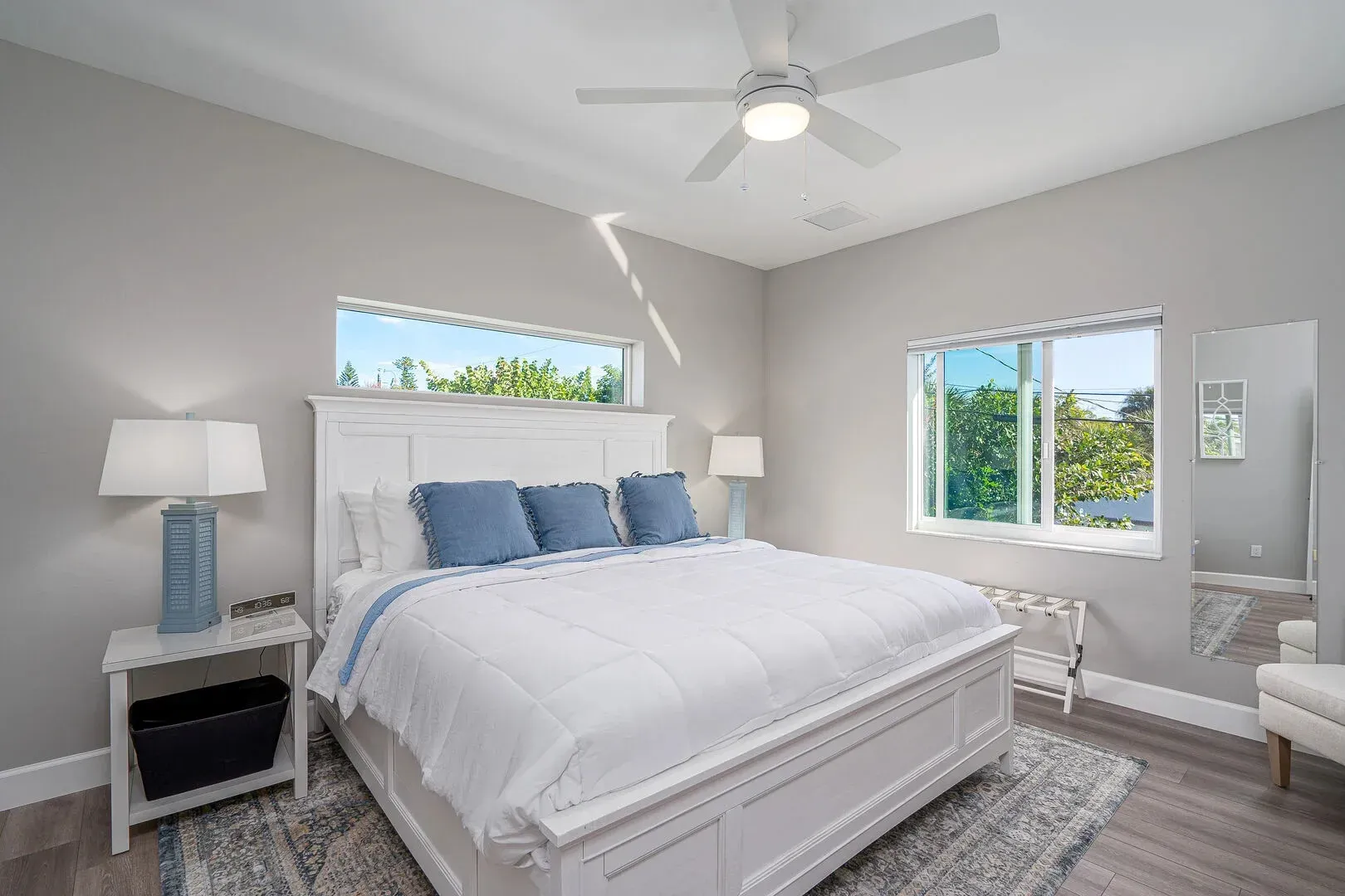 White bedroom with white bed, blue pillows and accents, and a ceiling fan.