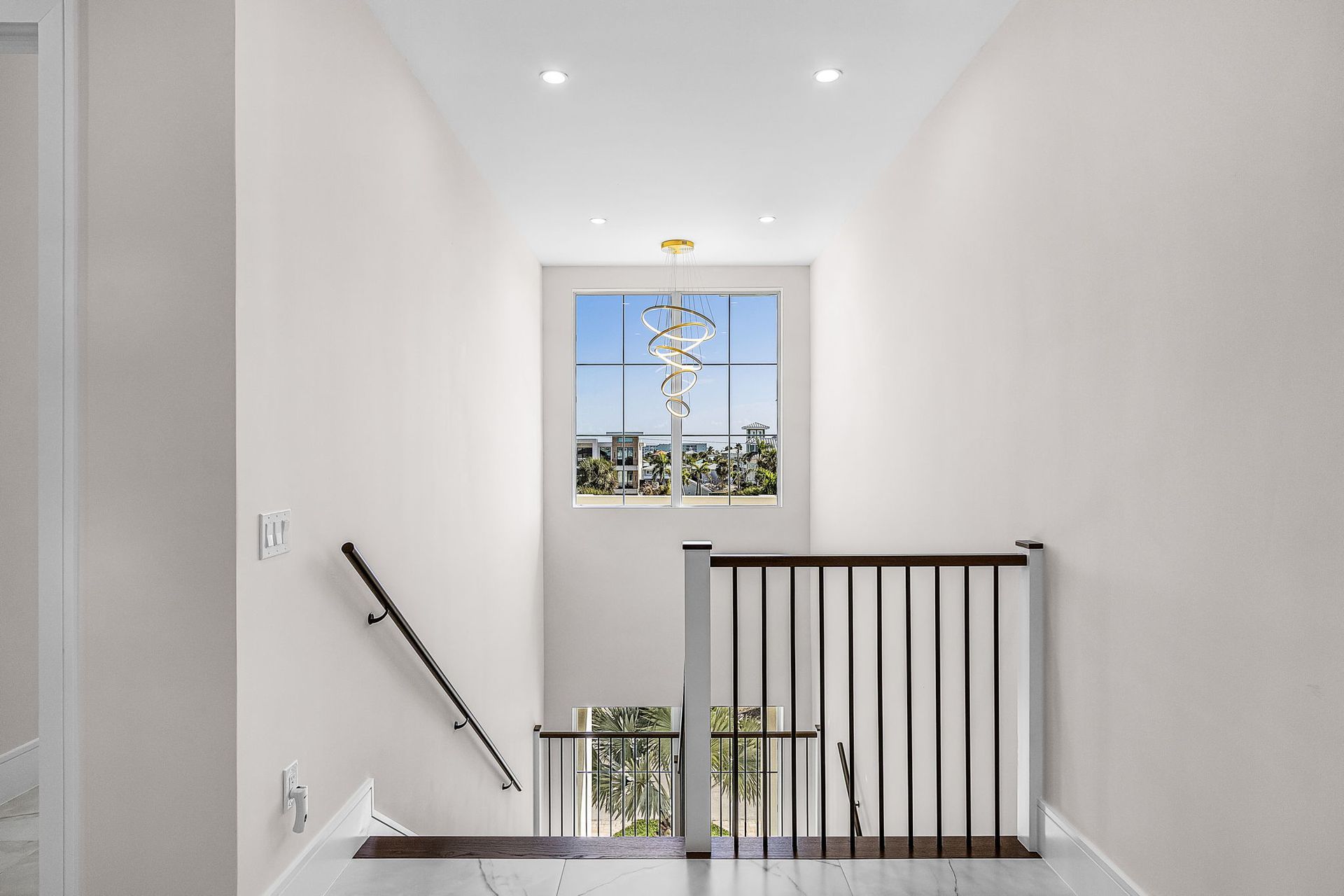 Hallway with stairs and window overlooking a tree-lined neighborhood. White walls, wood railing.