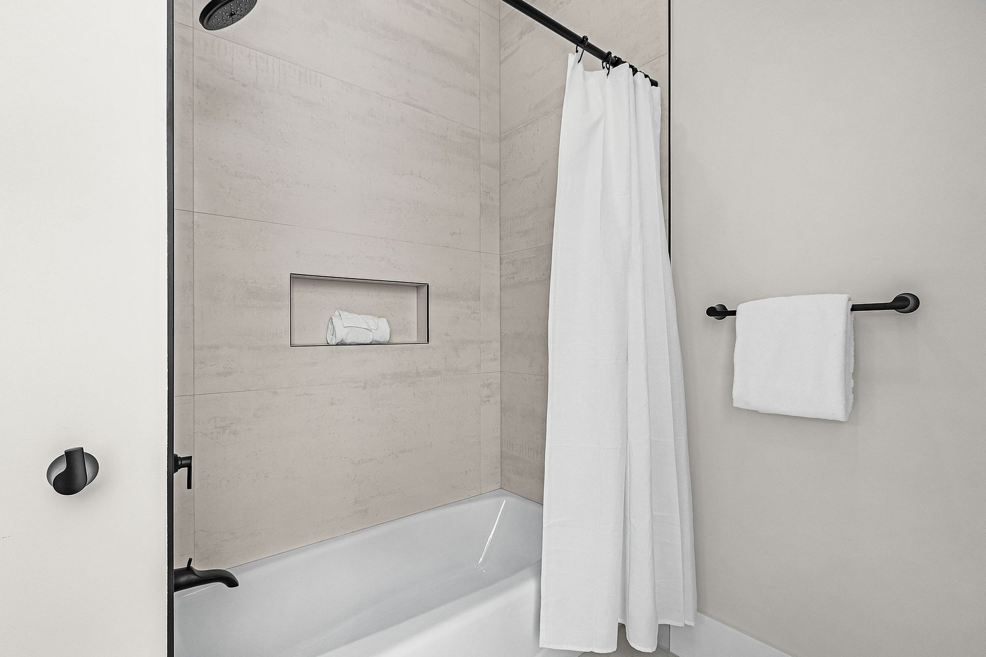 Bathroom with a white bathtub, light-colored tiled shower, and a white curtain. A towel hangs on a rod.