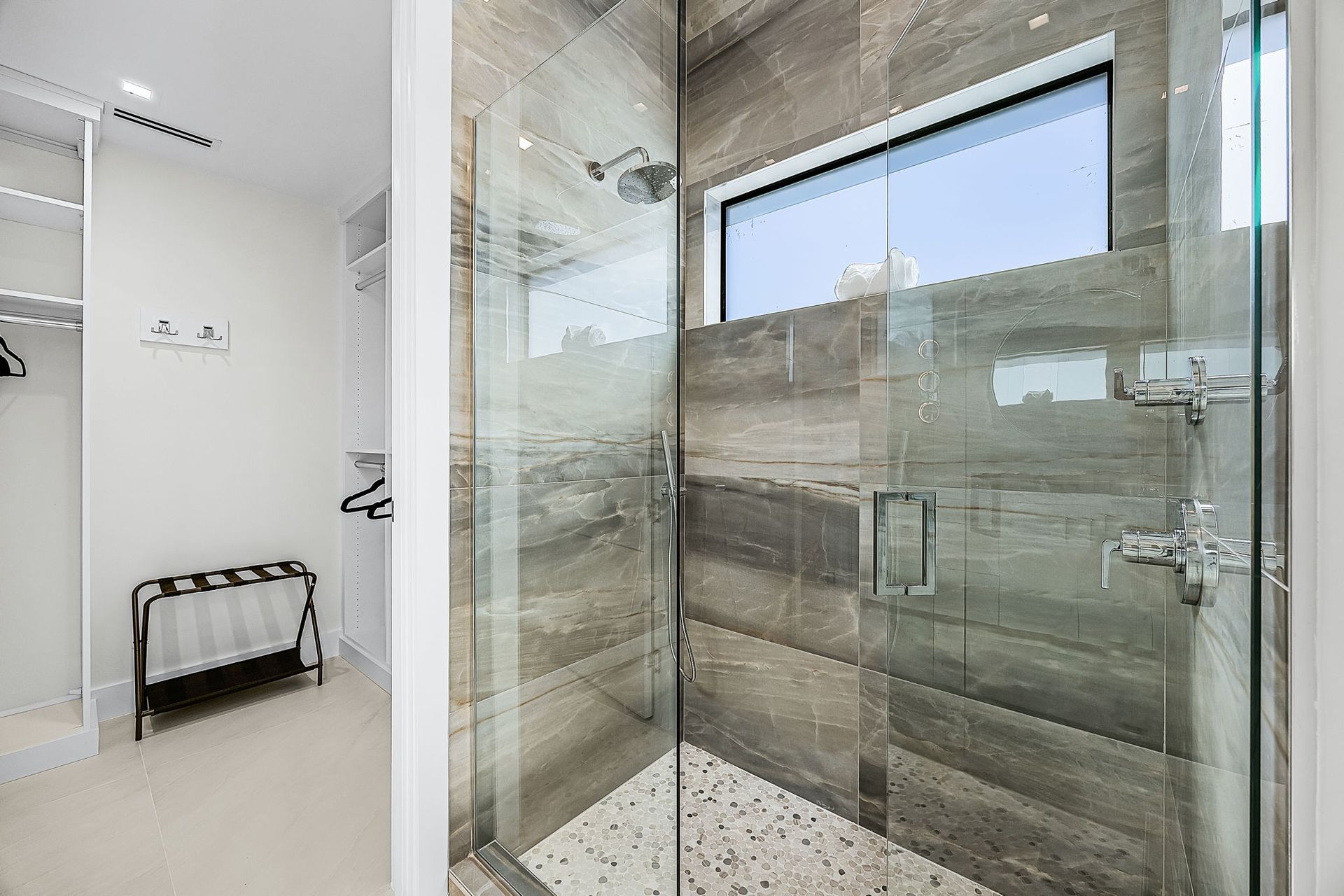 Modern bathroom with a glass shower, textured gray tile, and a small window.