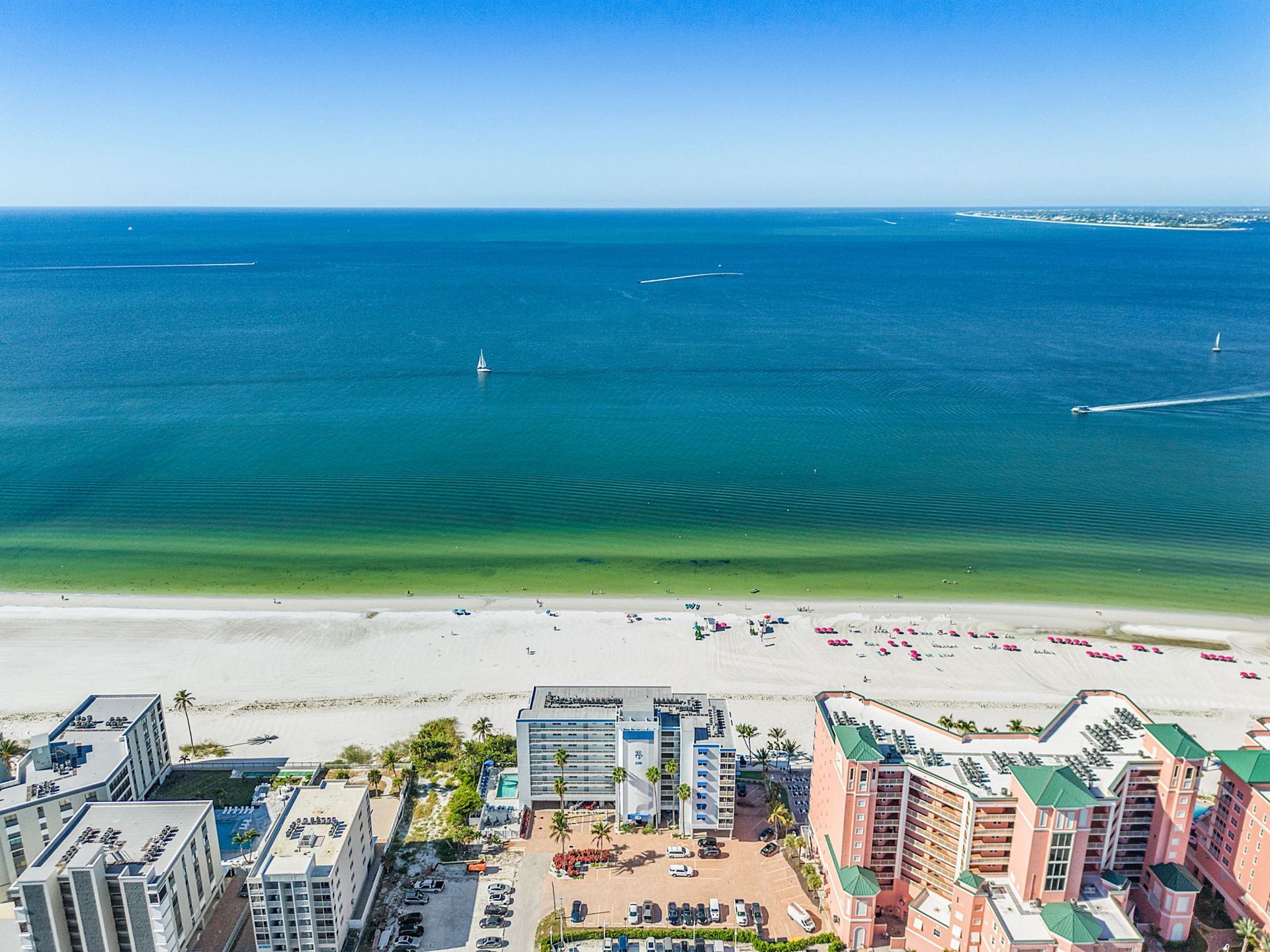 Aerial view of beach with buildings, white sand, and blue ocean.