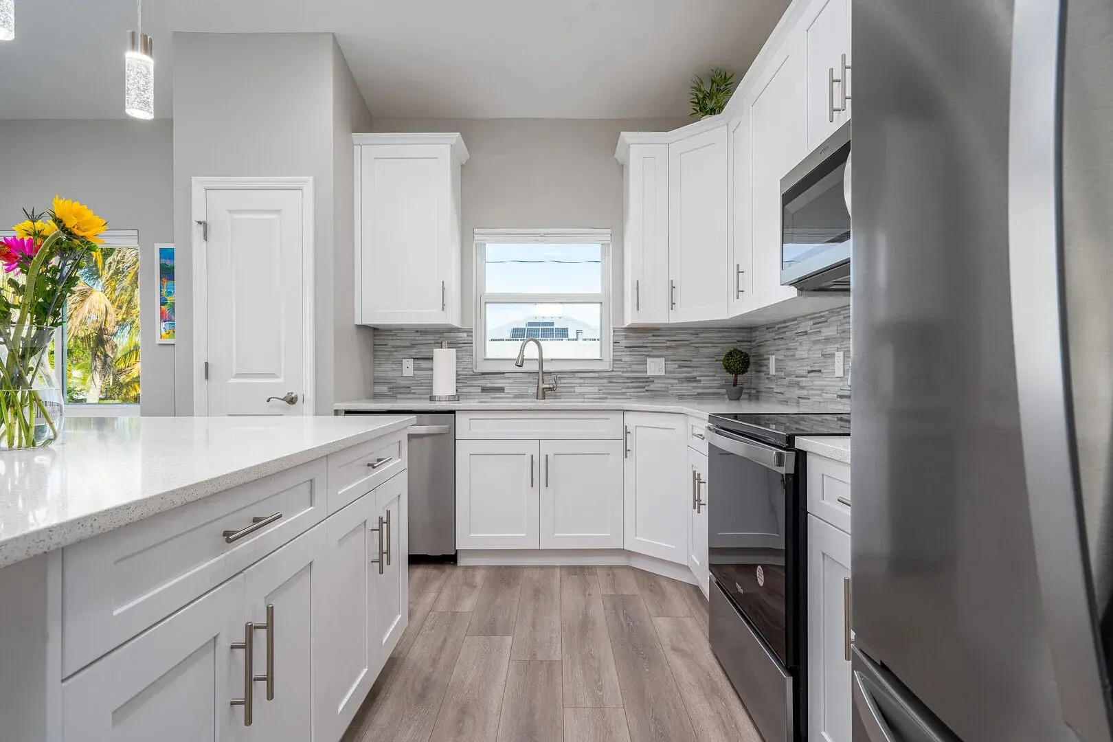 Bright, white kitchen with island, cabinets, stainless steel appliances, and a window.