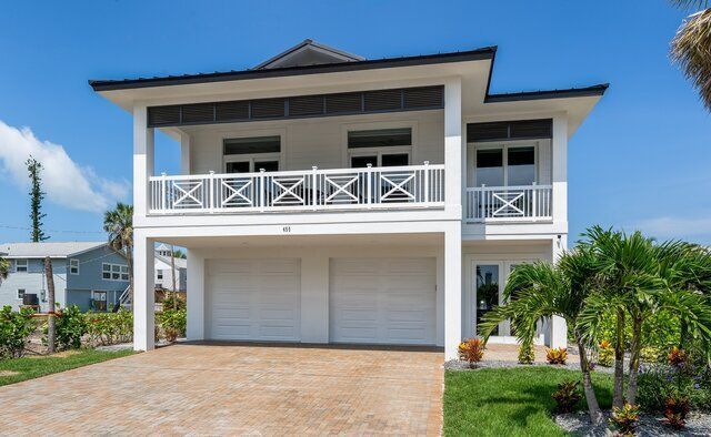 Two-story white house with a balcony over a two-car garage. Driveway, palm trees, and blue sky.