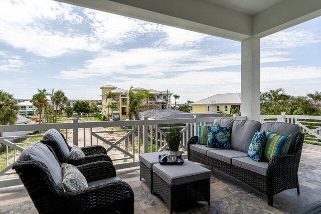 Balcony with gray wicker furniture, overlooking a neighborhood with houses and trees under a cloudy sky.