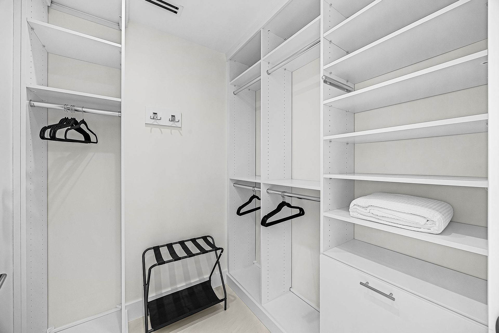 White walk-in closet with shelves, hanging rods, and a luggage rack. Empty, minimalist design.