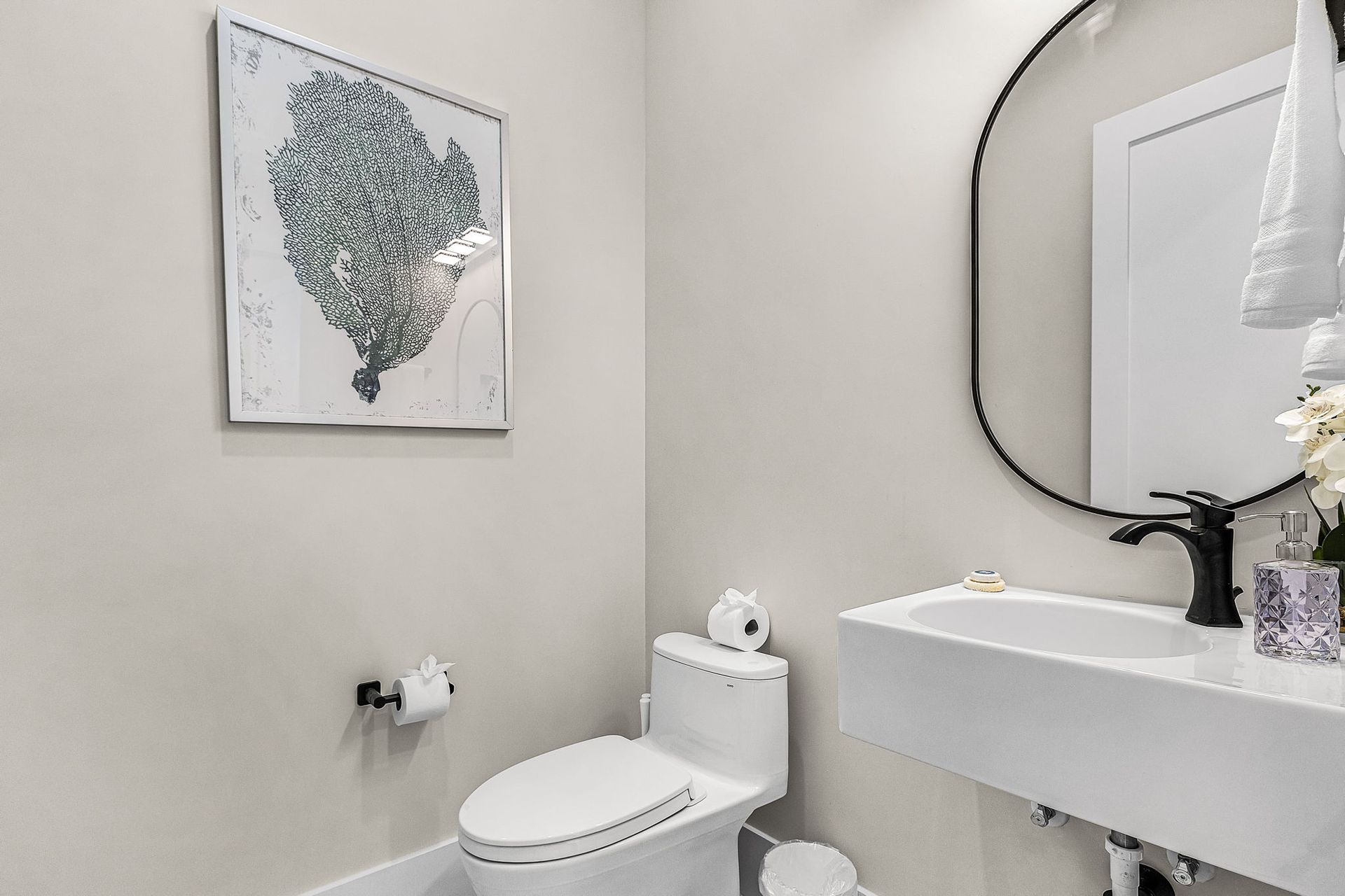 Modern powder room with white walls, toilet, floating sink, and round mirror.