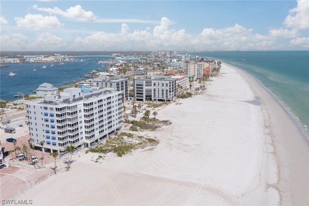Beachfront condos along white sand beach, blue water, boats, and sunny sky.