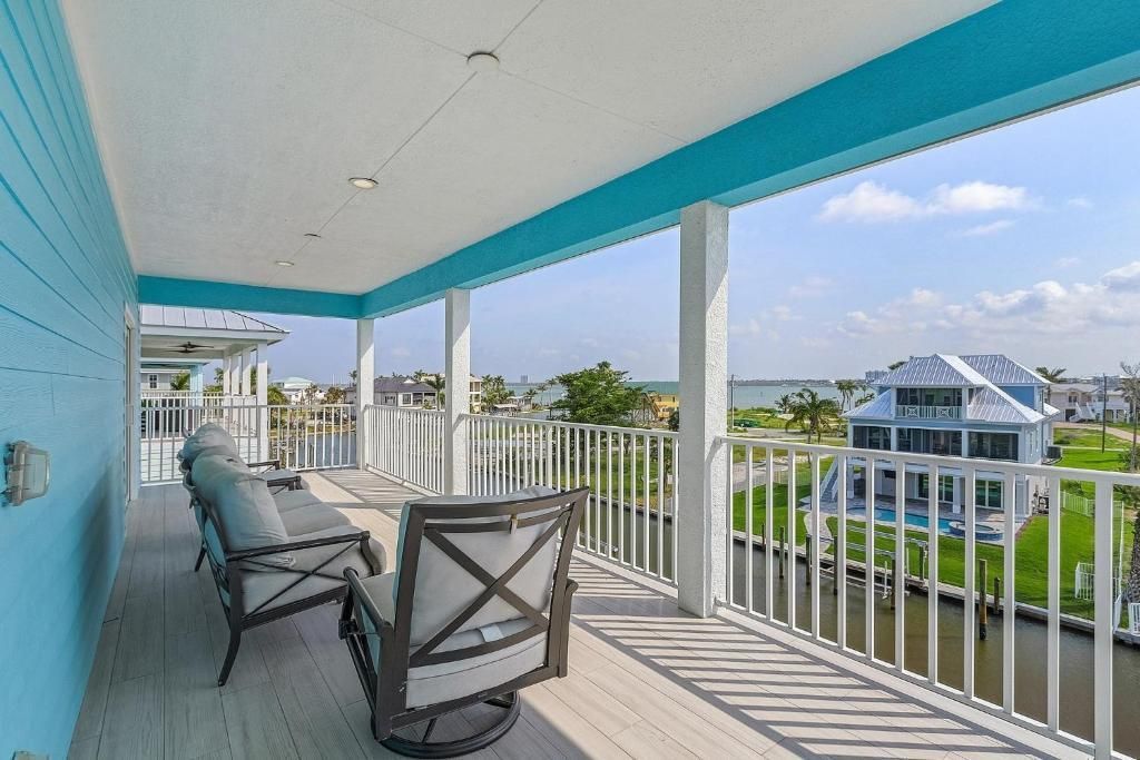 Balcony with seating, overlooking water and homes, light blue trim and a sunny day.