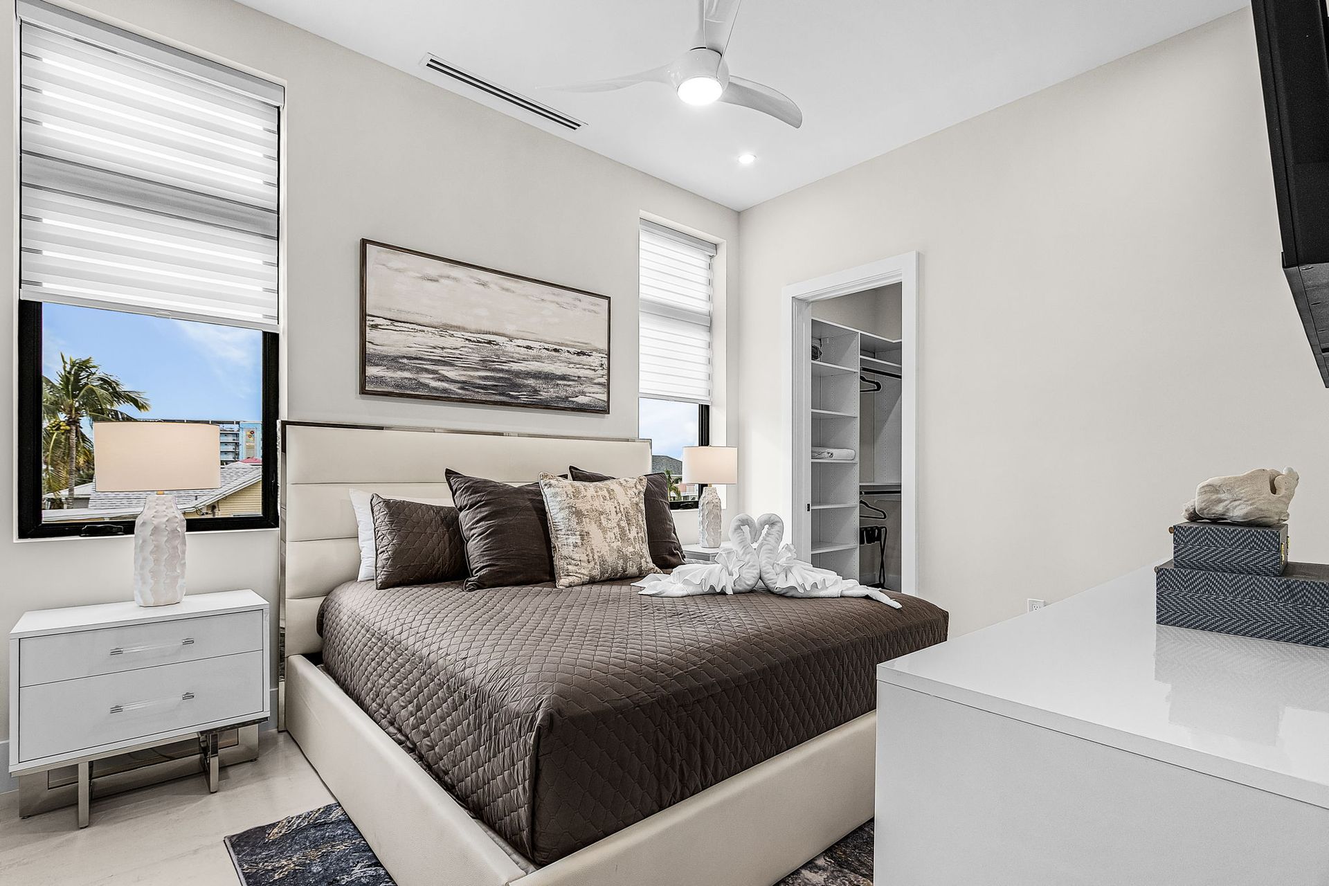 Bedroom with a bed, dresser, windows, and a walk-in closet. Light walls, neutral colors, and modern decor.
