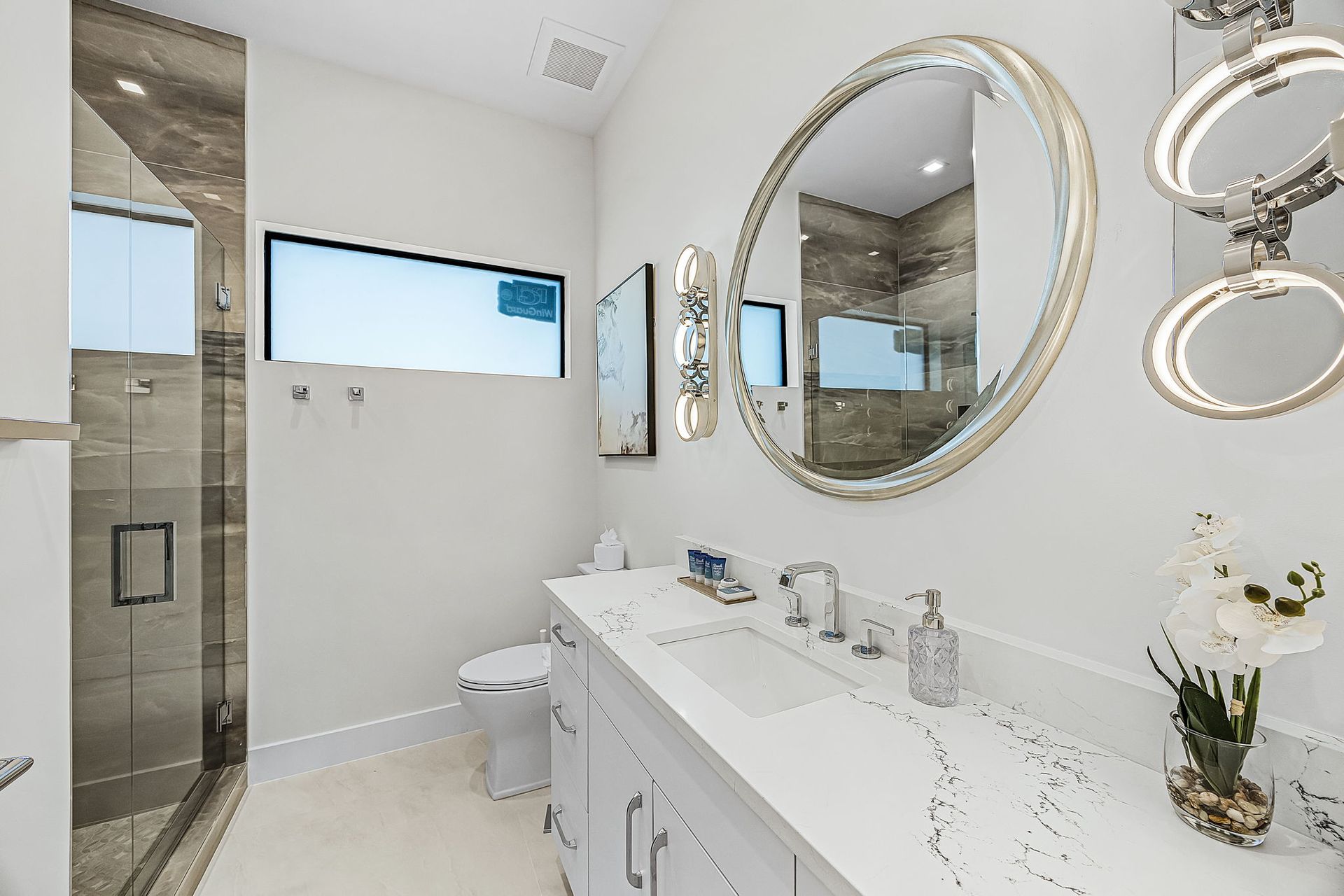 Bathroom with white cabinets, marble countertop, large mirror, and glass shower.