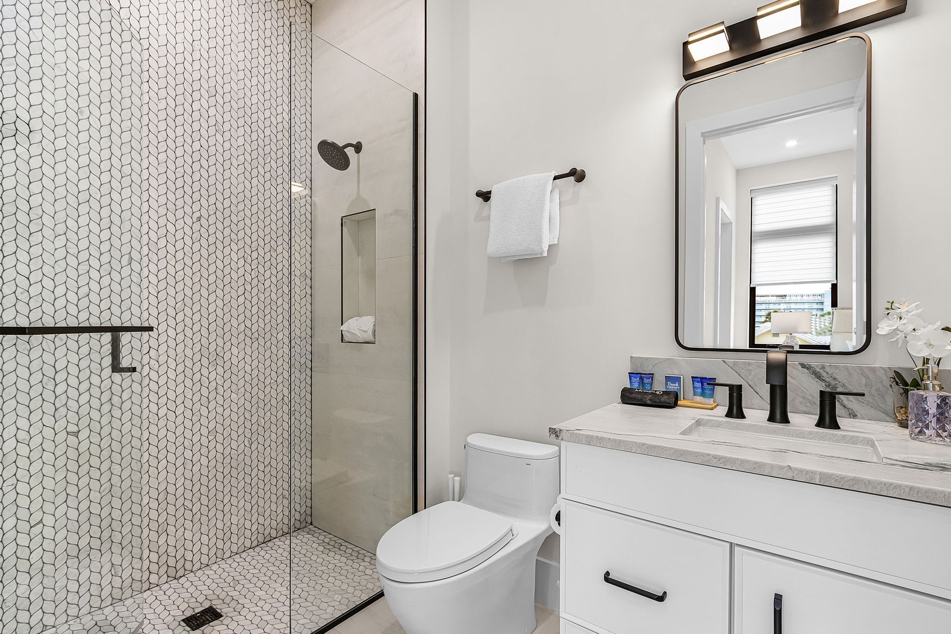 Modern bathroom with a glass-enclosed shower, white vanity, toilet, mirror, and dotted tile wall.