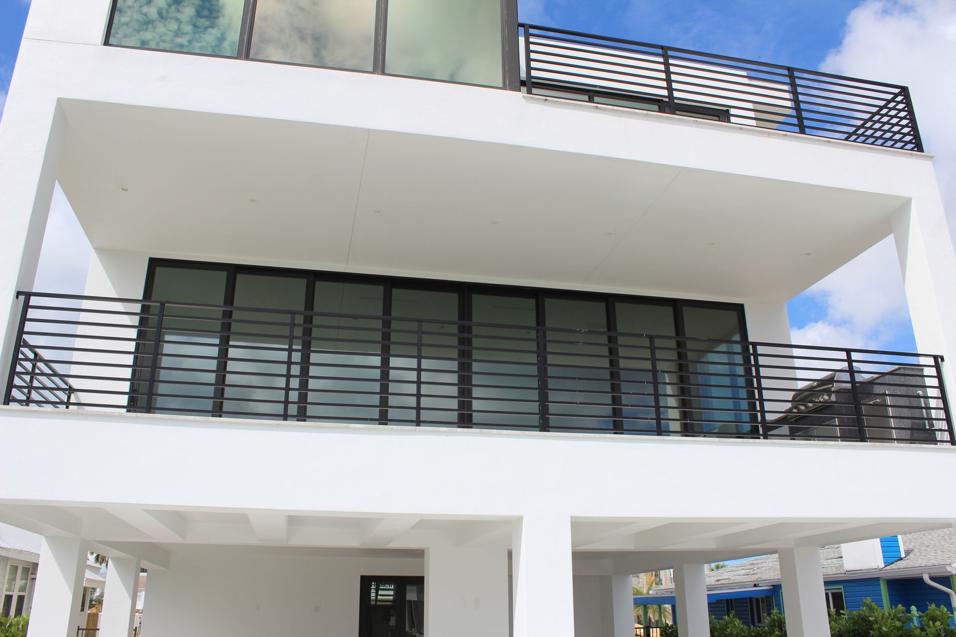 White modern multi-story building with black railing, large windows, and a balcony.