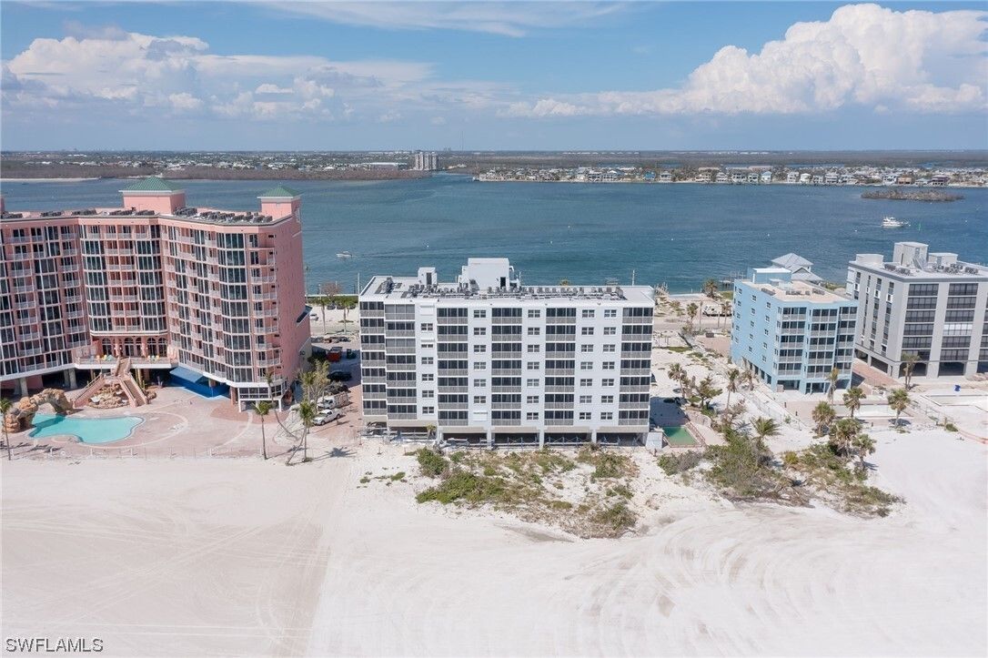 Beachfront buildings after a storm; ocean, white sand, and blue sky in background.