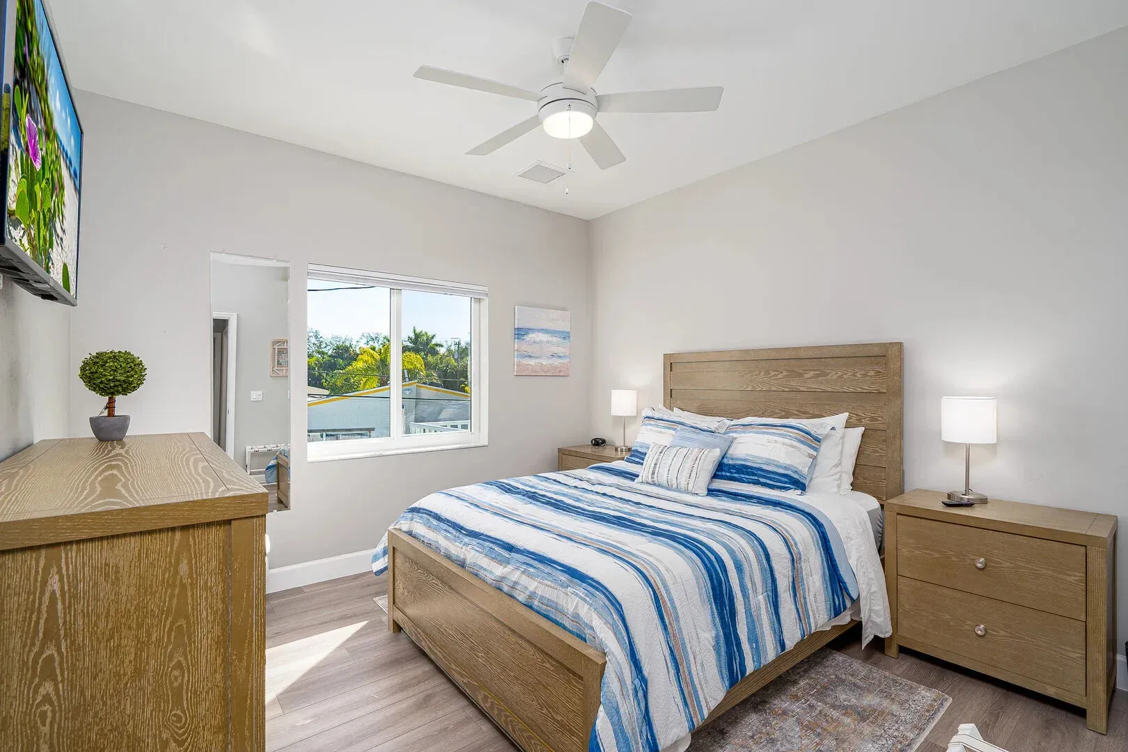 Bedroom with a bed, dresser, nightstands, window, and ceiling fan. Blue and white striped bedding.