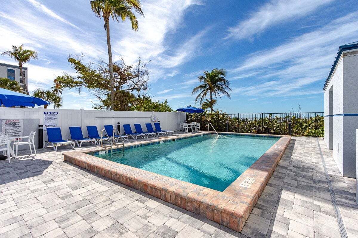 Pool with lounge chairs, brick edge, and ocean view on a sunny day.