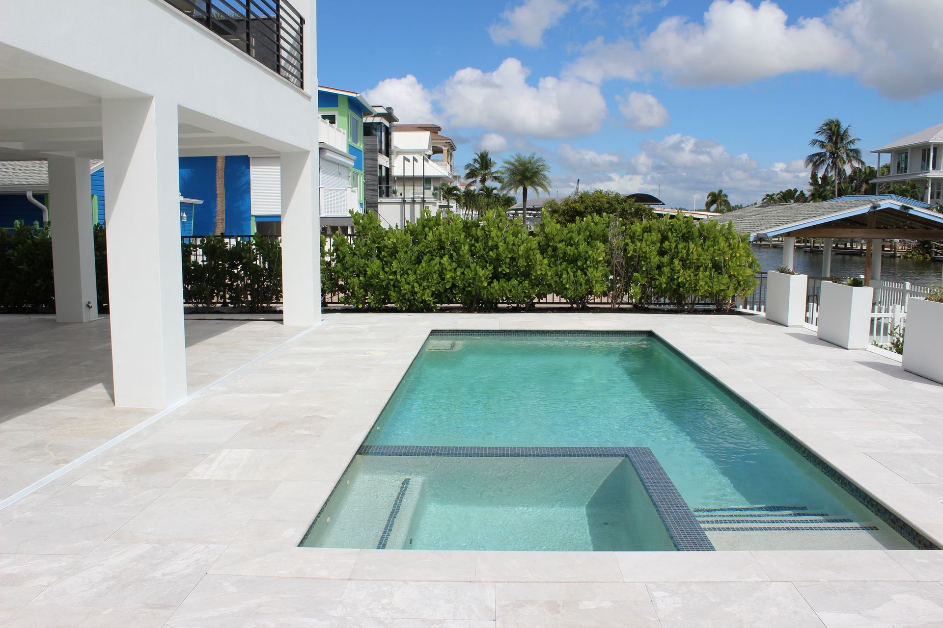 Pool and spa next to a white house with blue accents on a sunny day.