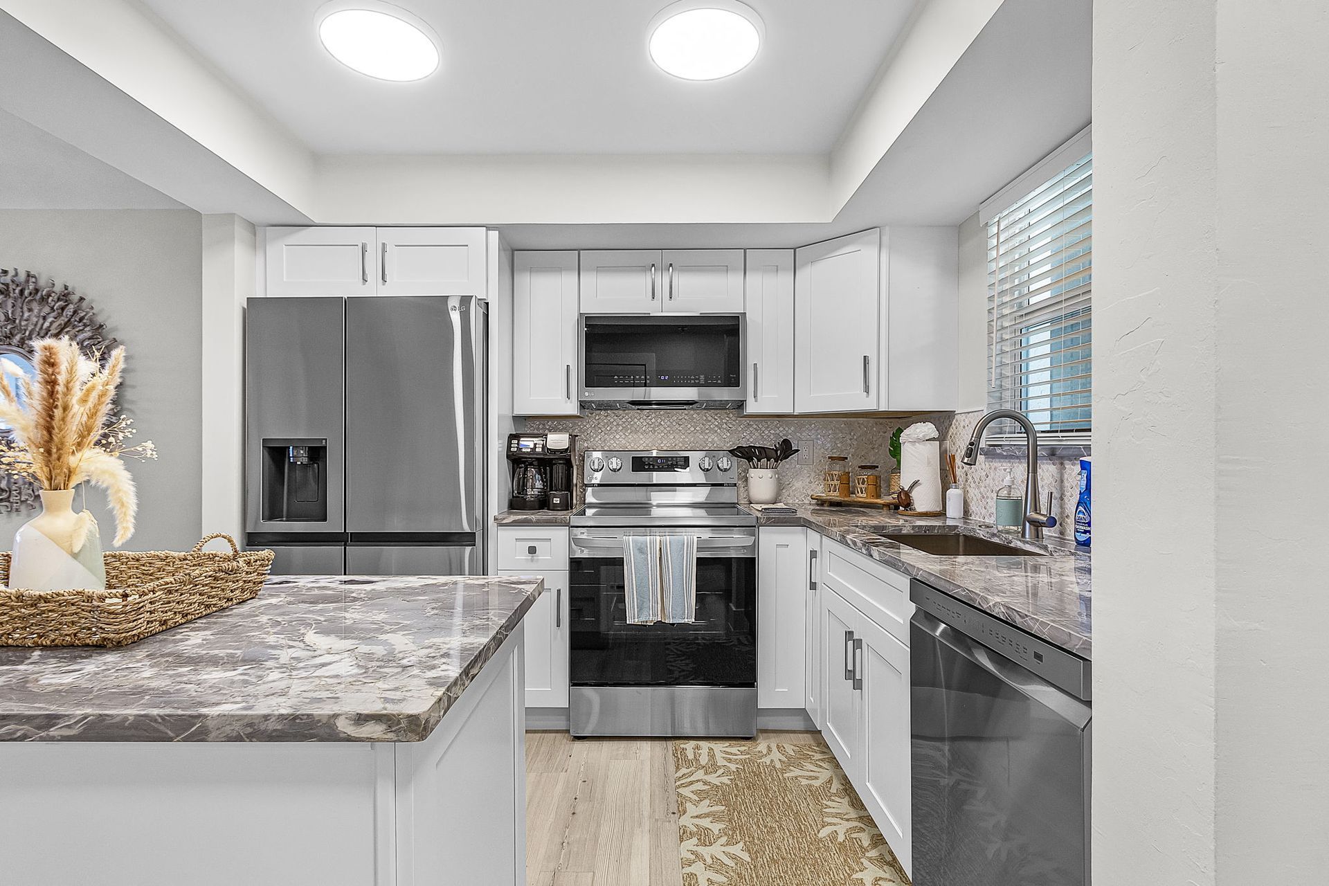 Modern white kitchen with stainless steel appliances, granite countertops, and light wood floors.