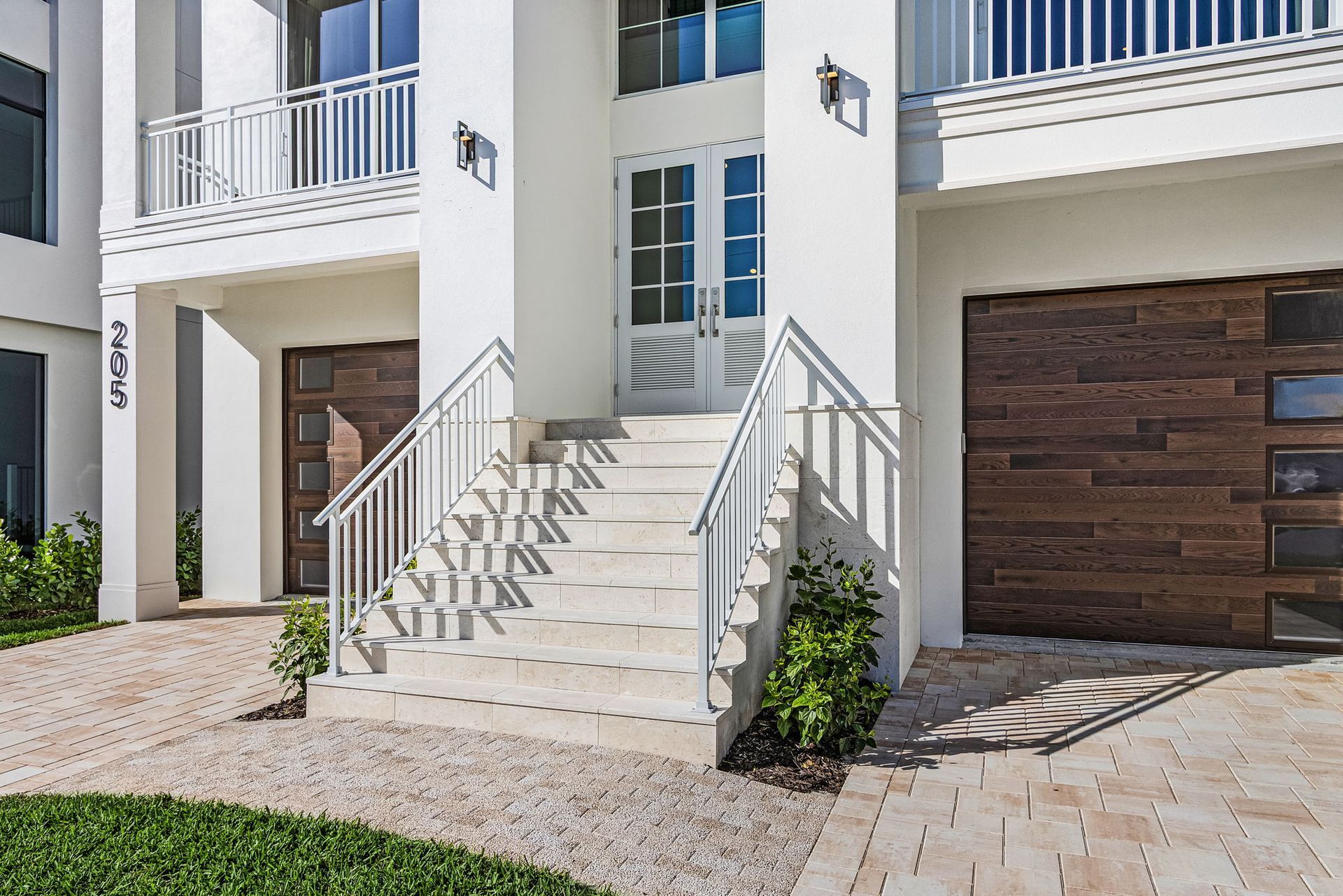 White modern home with stairs to a double door entry, flanked by garages with wood doors.