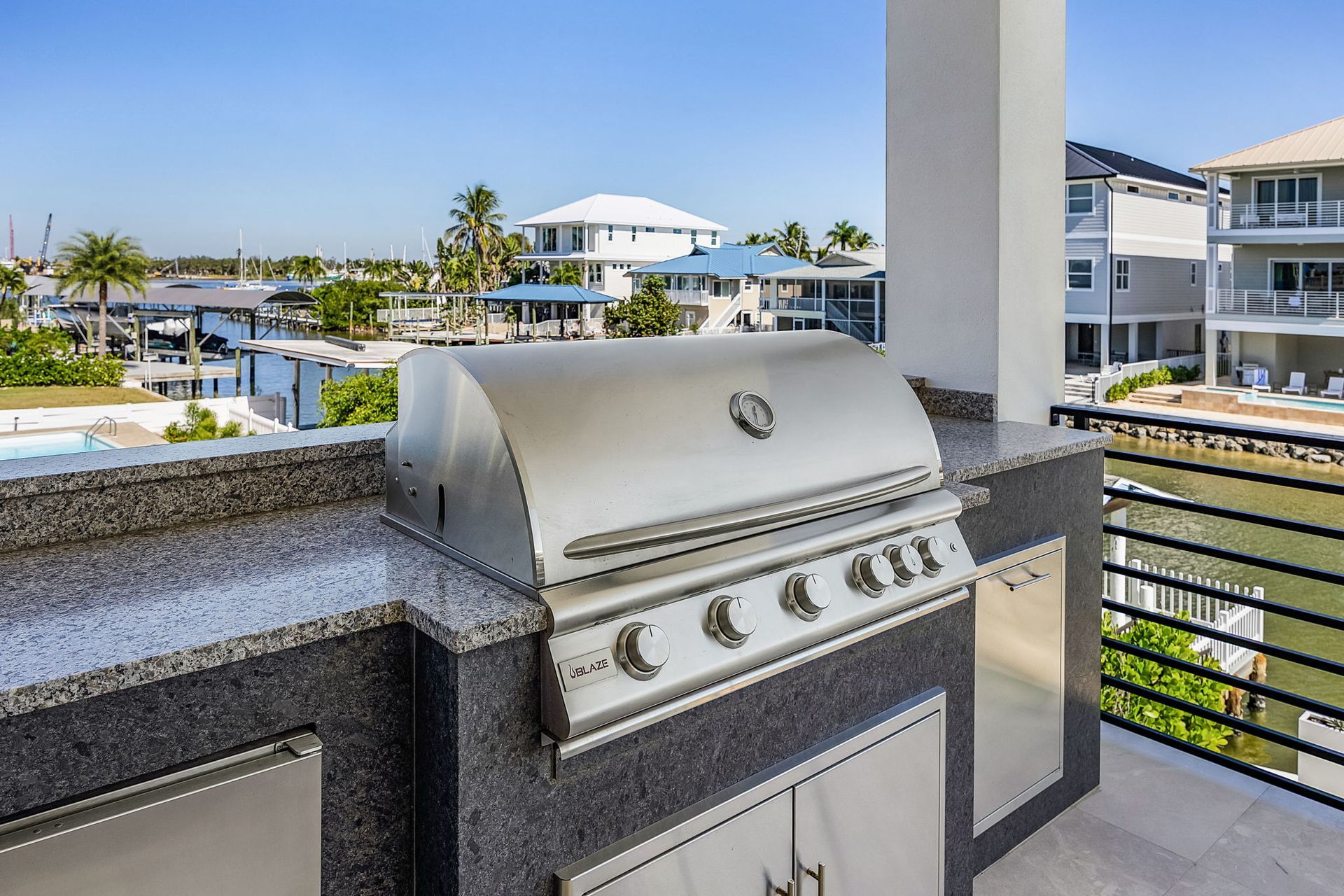 Outdoor grill with stainless steel hood and granite counter overlooking a waterfront view.