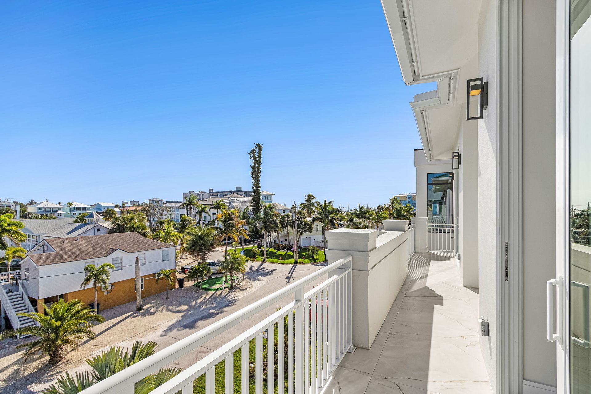 Balcony view overlooking a street with buildings, palm trees, and clear blue sky.