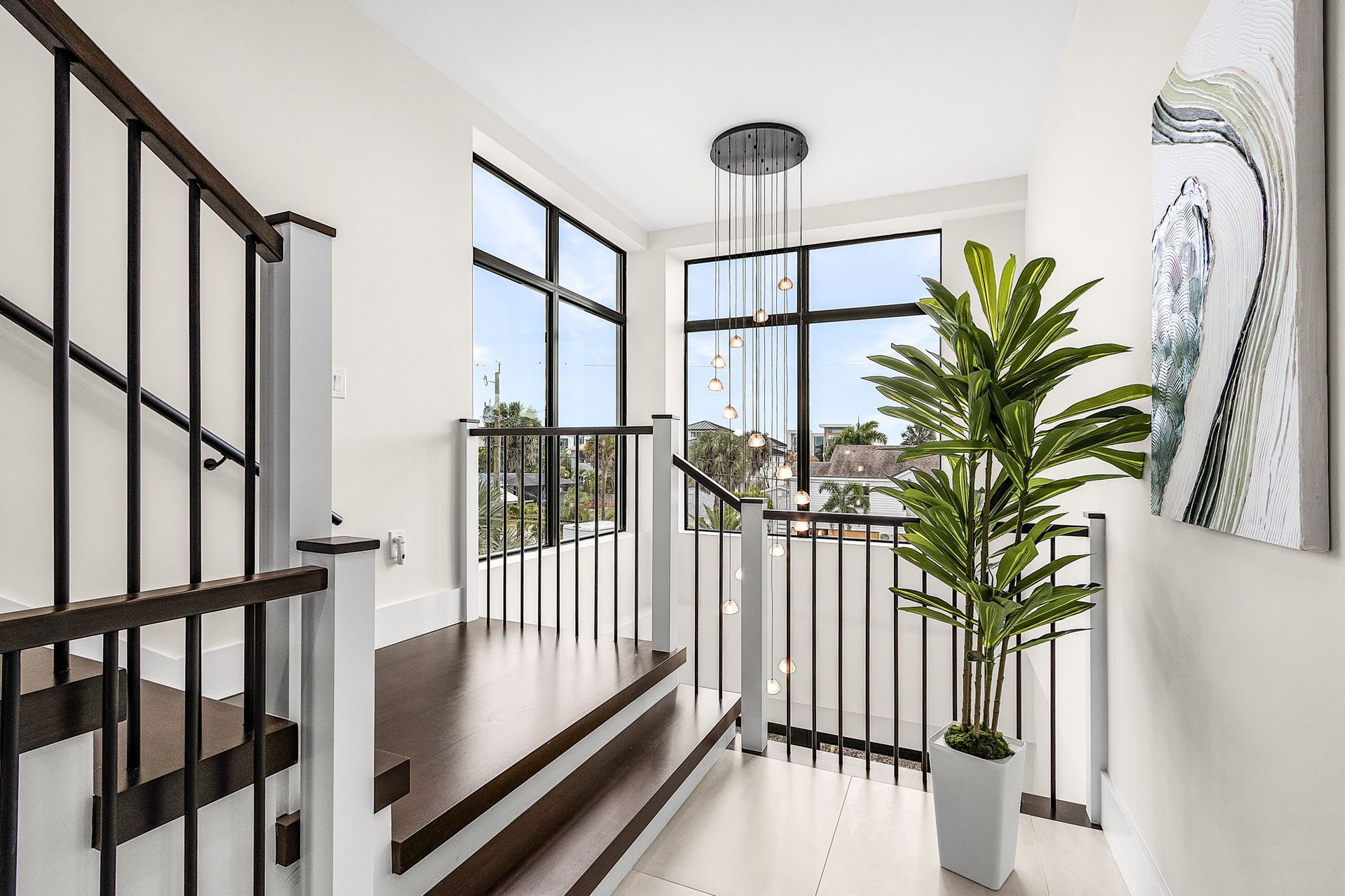 Staircase with dark wood steps and black and white railings, large windows, and a tall potted plant.
