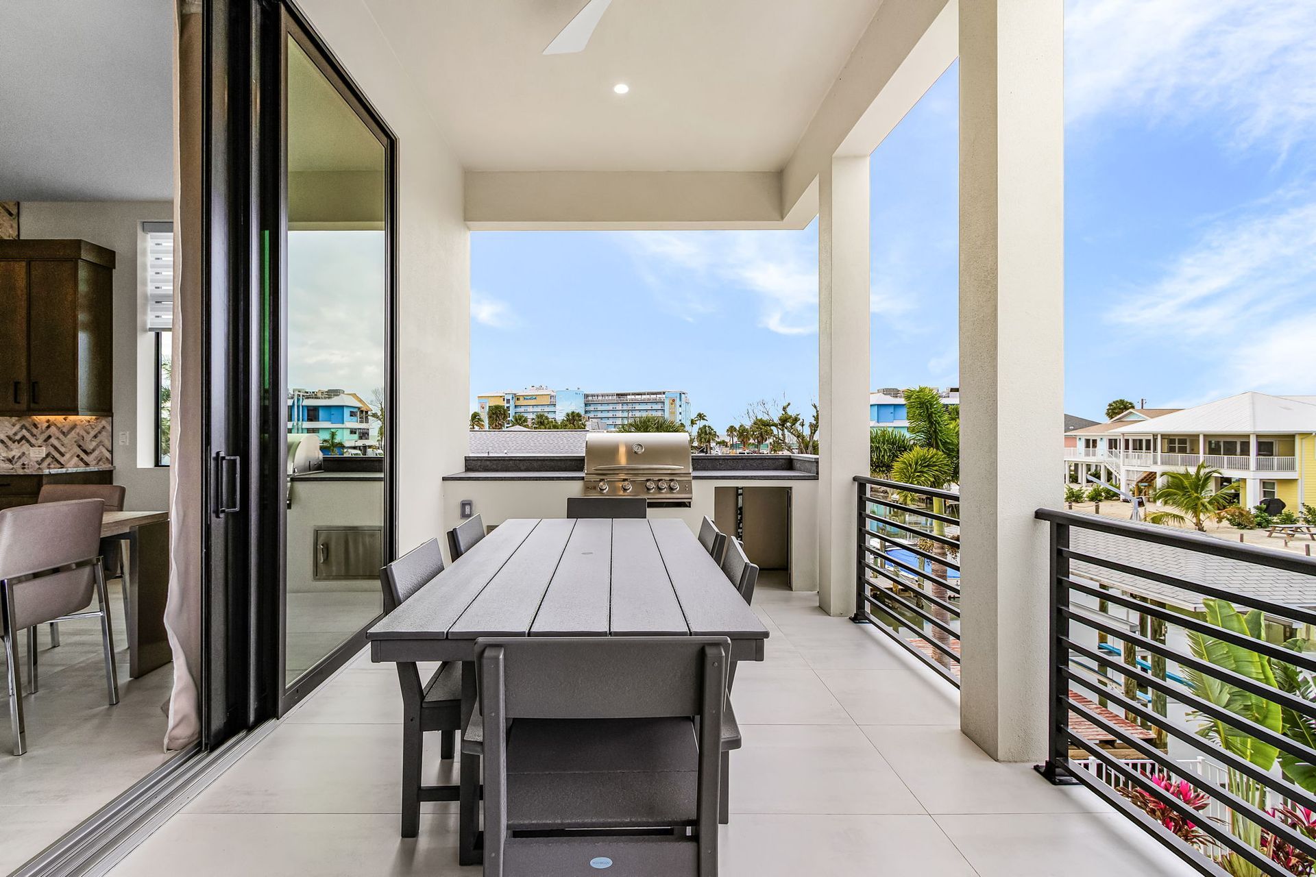 Patio with dining table, grill, and view of buildings and blue sky.
