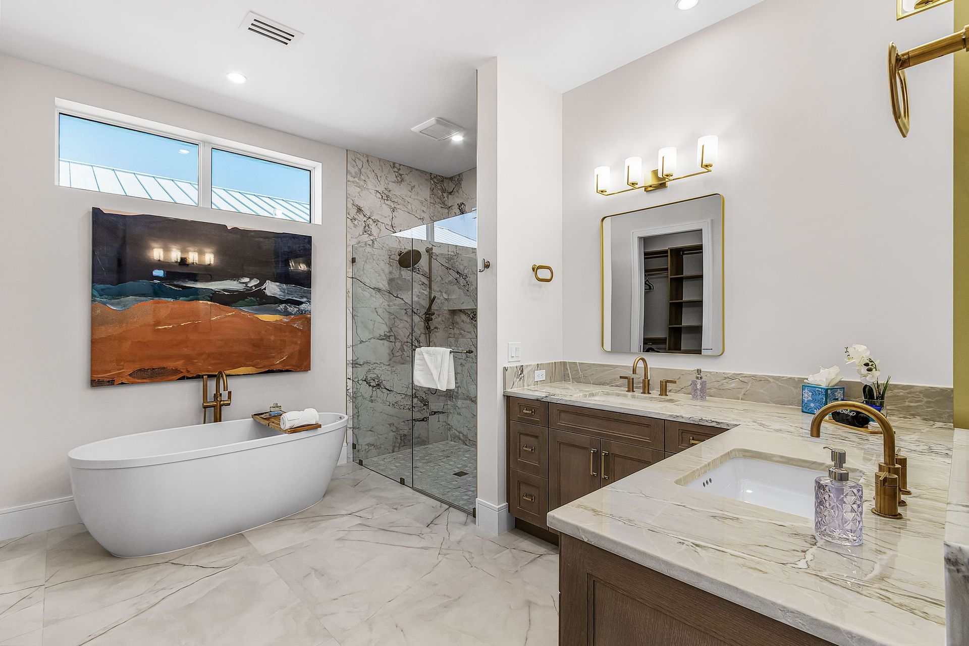 Luxurious bathroom with soaking tub, glass shower, double vanity, artwork, and gold fixtures.