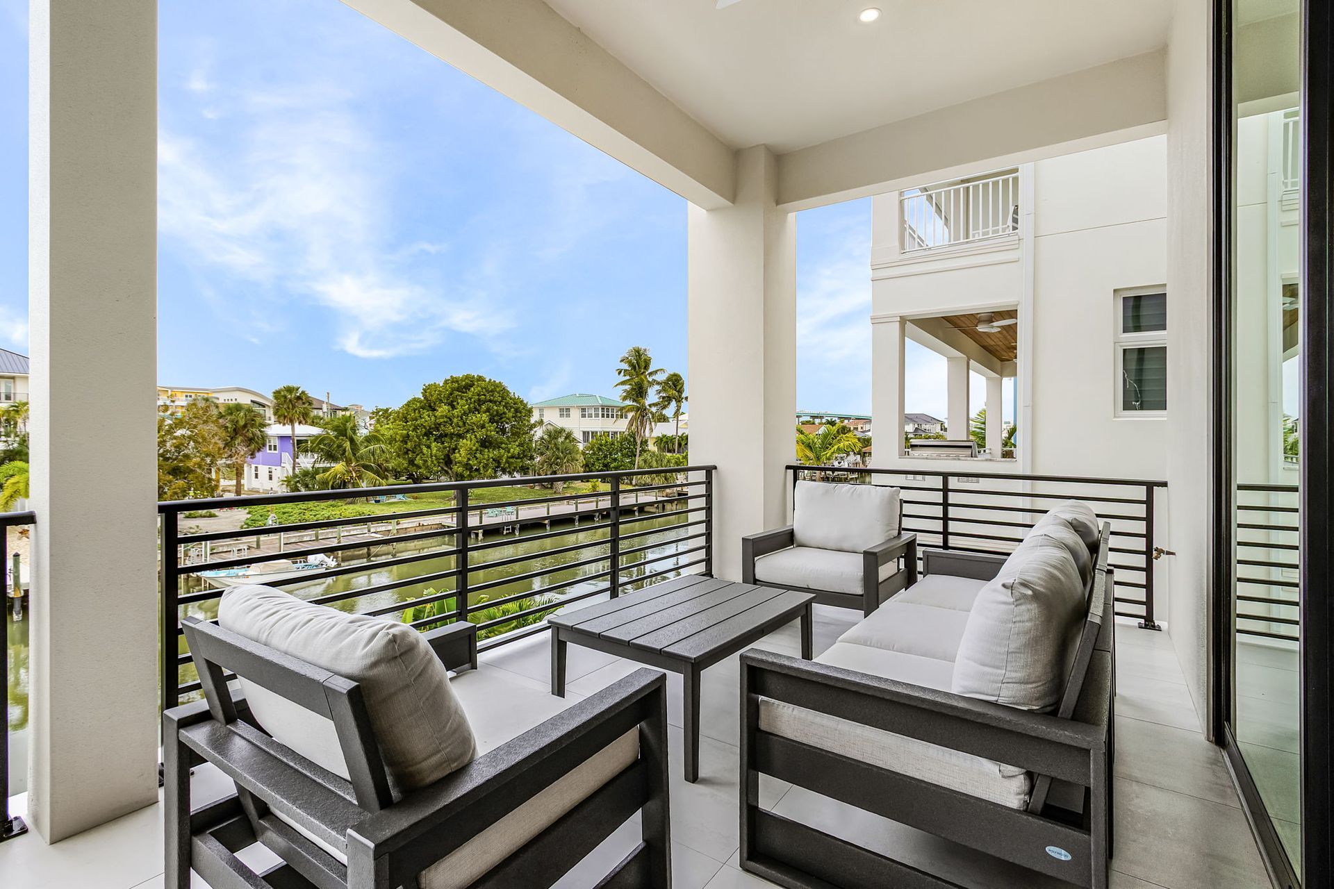 Balcony with gray outdoor furniture overlooking a neighborhood with blue sky.