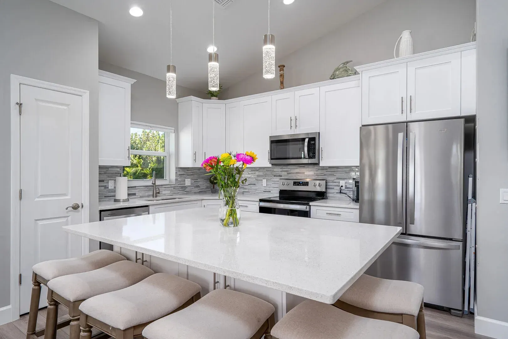 White kitchen with island, stainless steel appliances, and pendant lights.