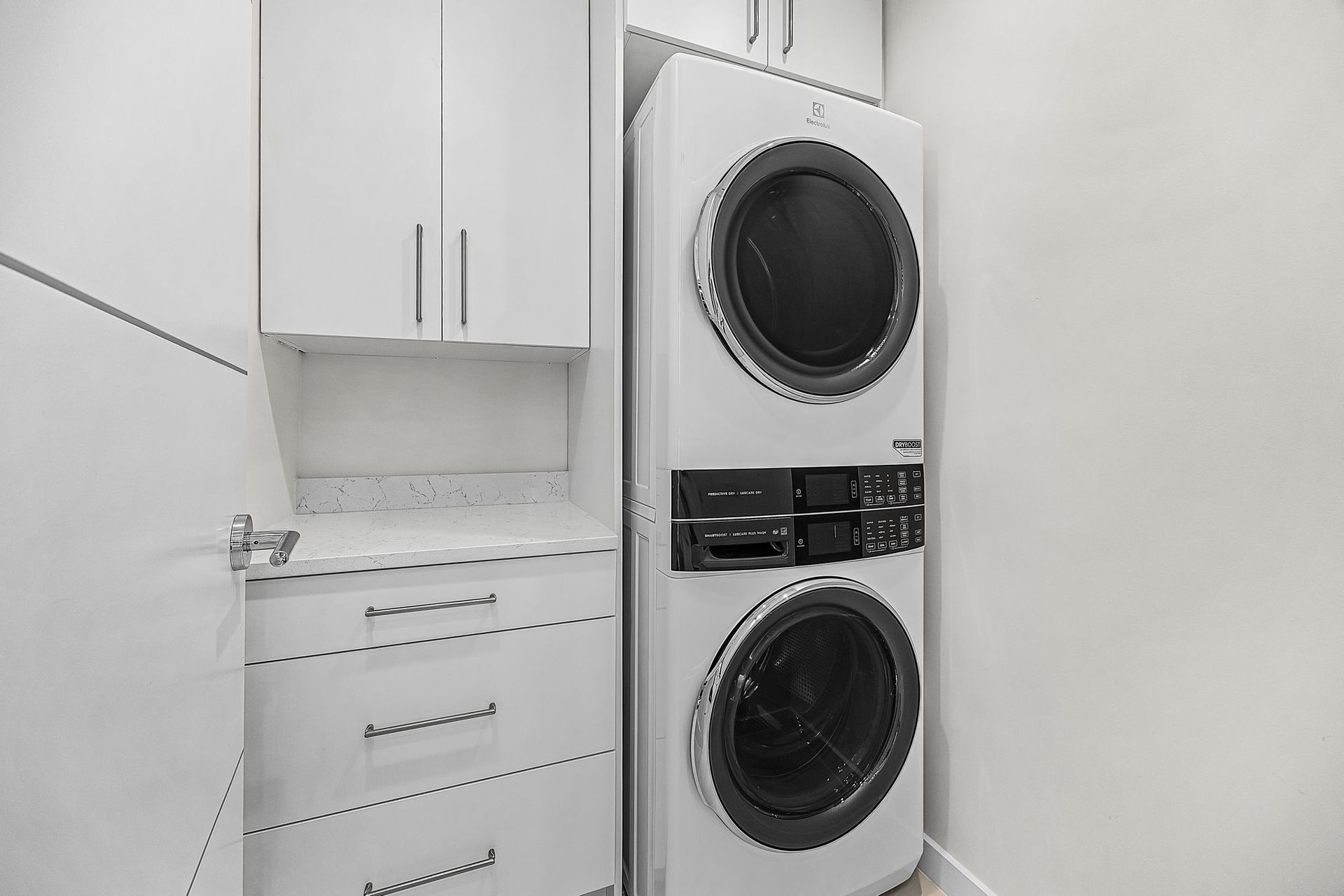 White stacked washer and dryer in a small laundry room with white cabinets and countertop.