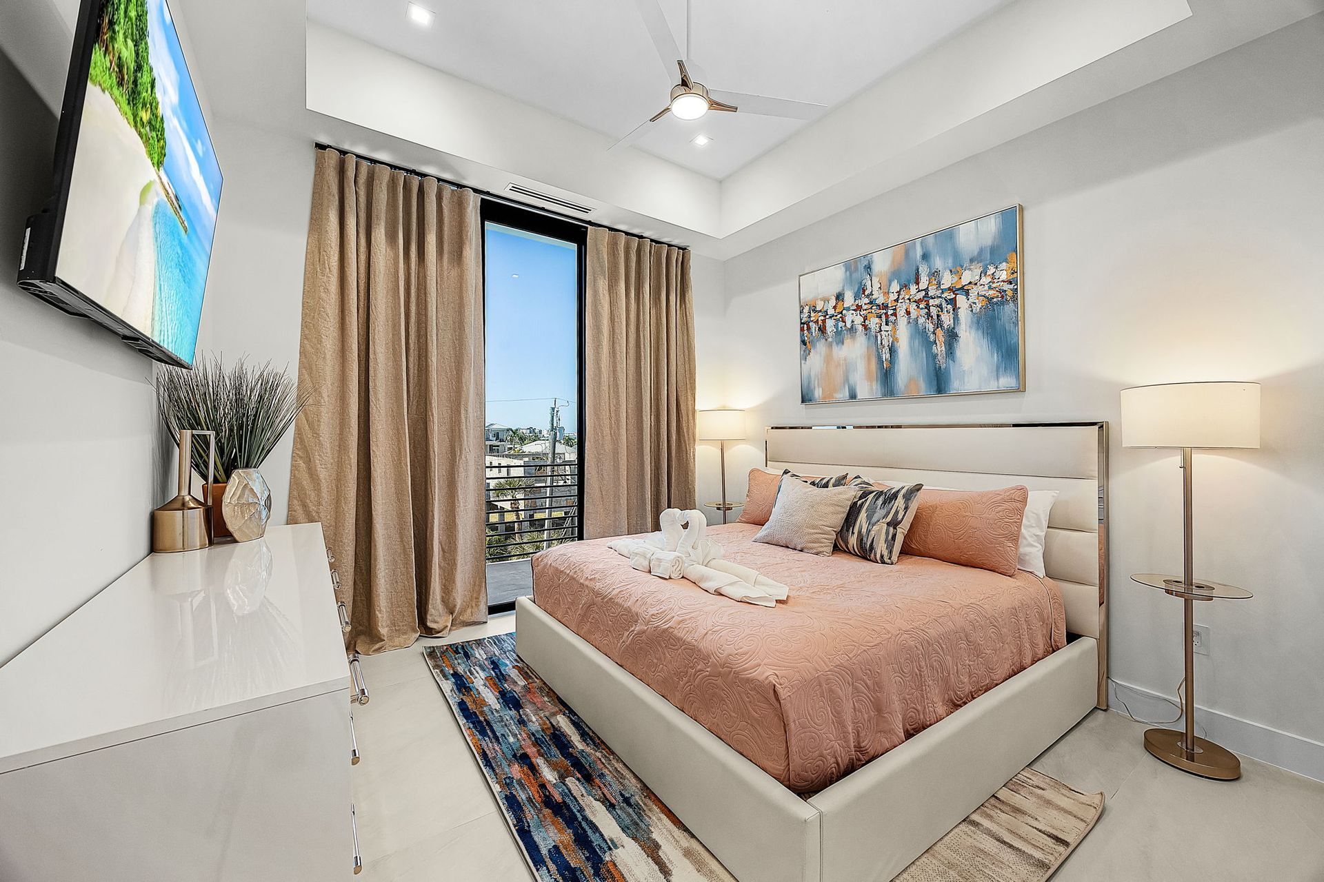 Elegant bedroom with bed, artwork, large window, and cream and gold color scheme.