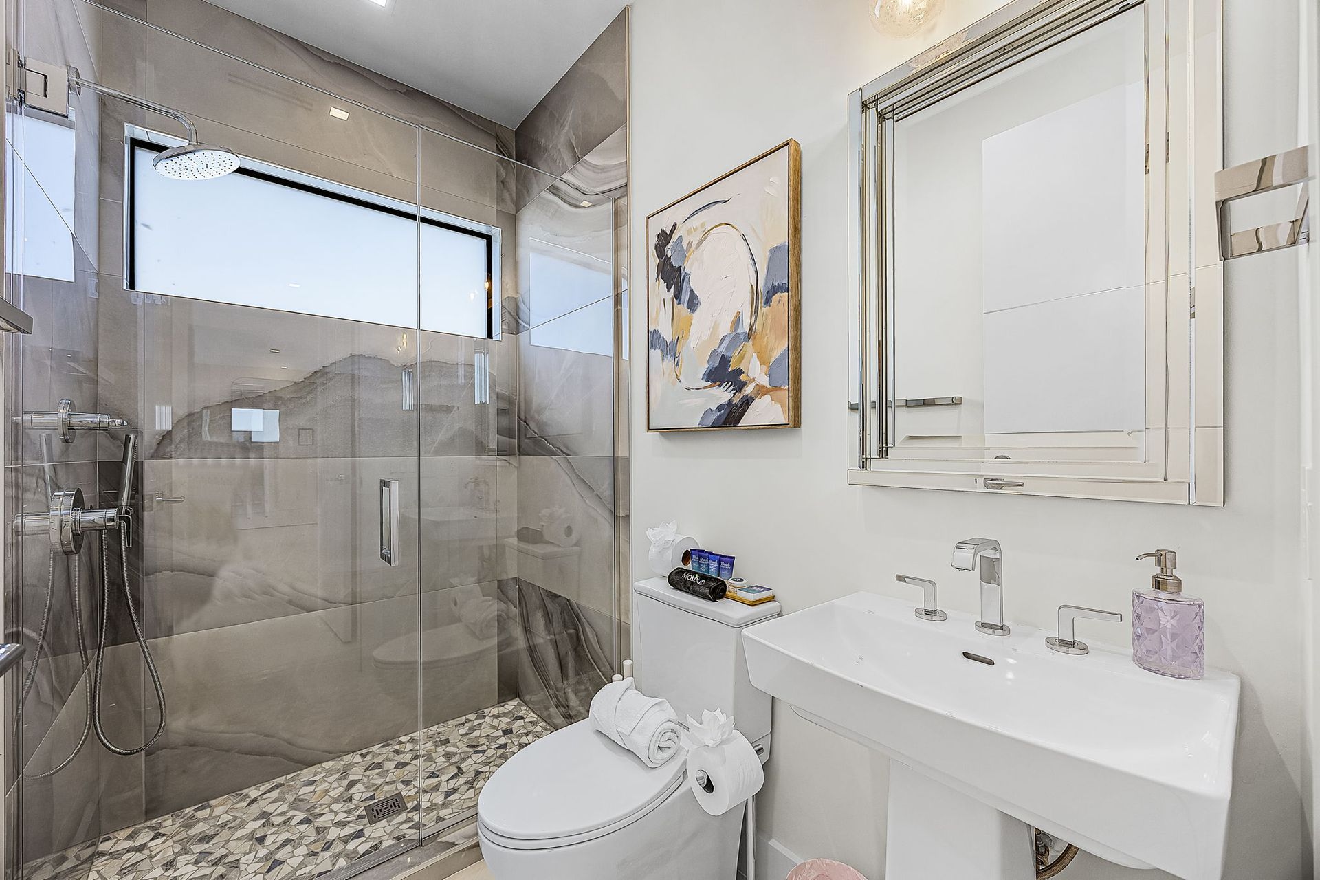 Modern bathroom with glass shower, pedestal sink, and artwork.