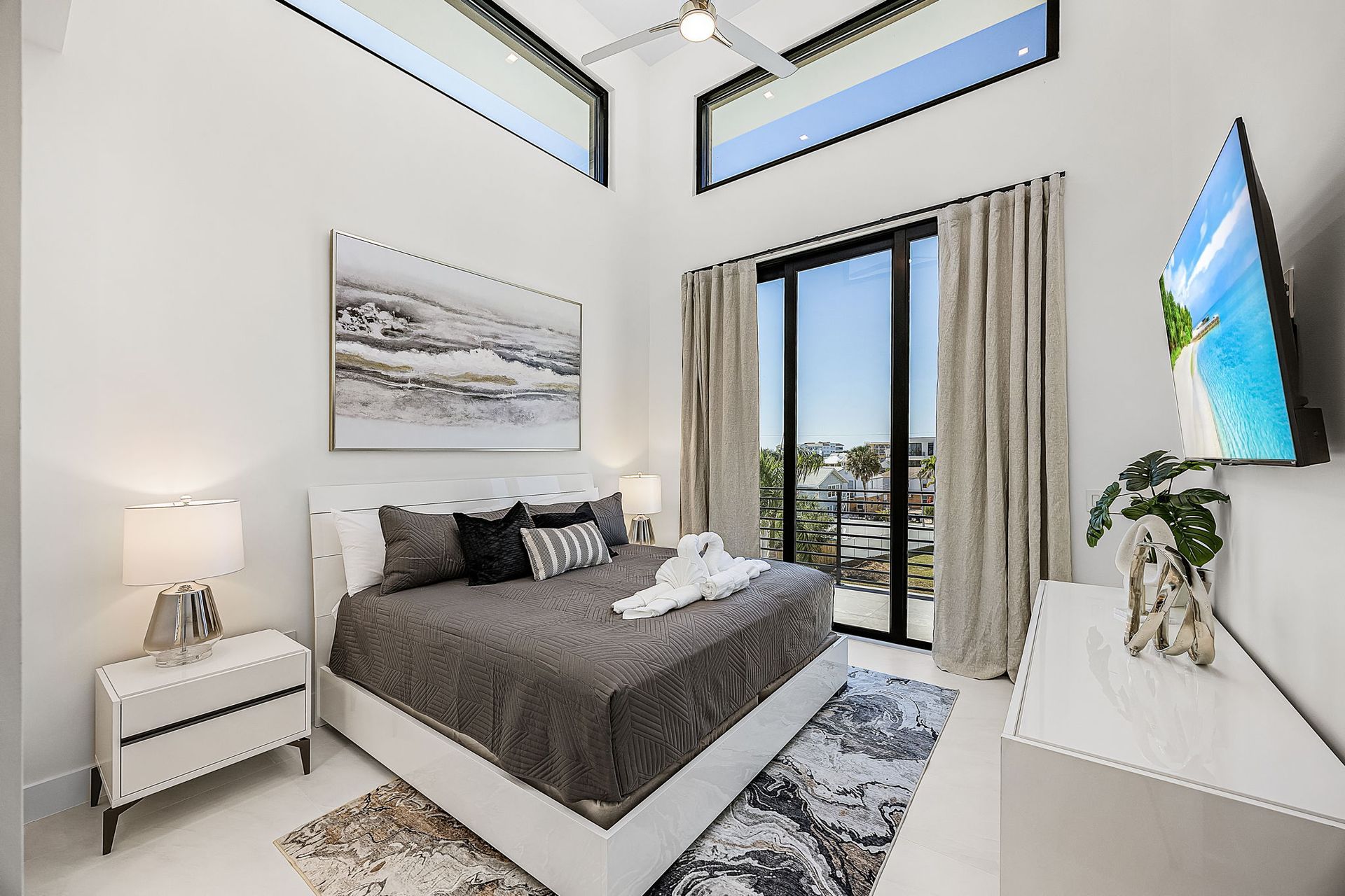 Bedroom with king bed, balcony, neutral colors, modern decor, and TV.