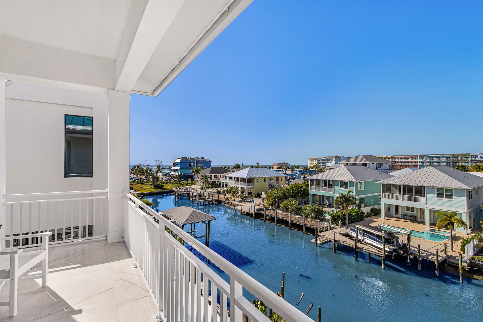 Balcony view overlooking a canal with houses, docks, and blue water under a clear sky.