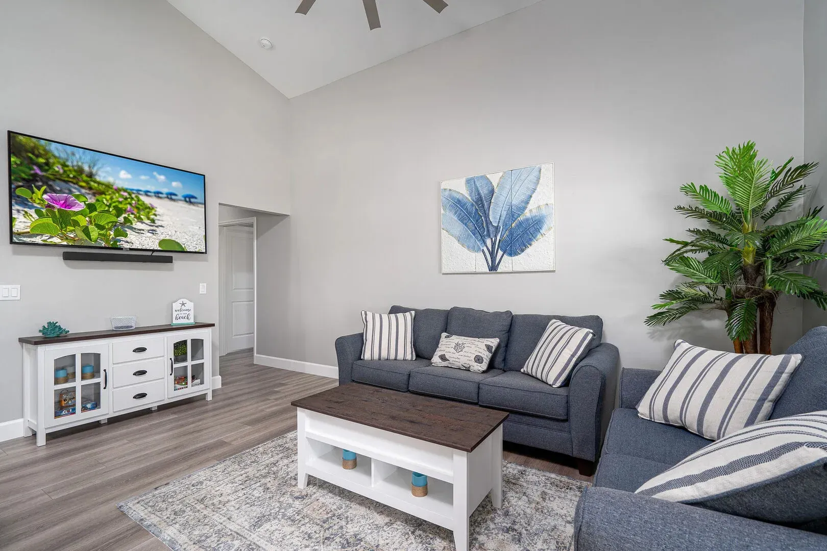 Living room with blue sofa, white console, mounted TV, and artwork.