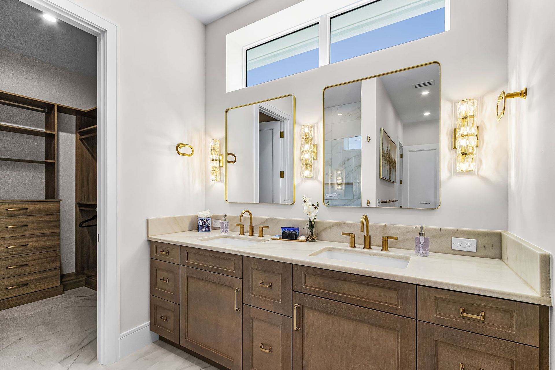 Bathroom with double vanity, two mirrors, gold fixtures, and a walk-in closet.