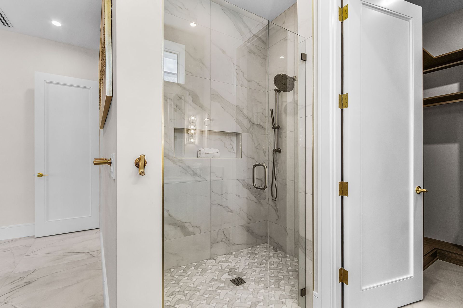 Luxury bathroom with marble shower, gold hardware, and white doors.