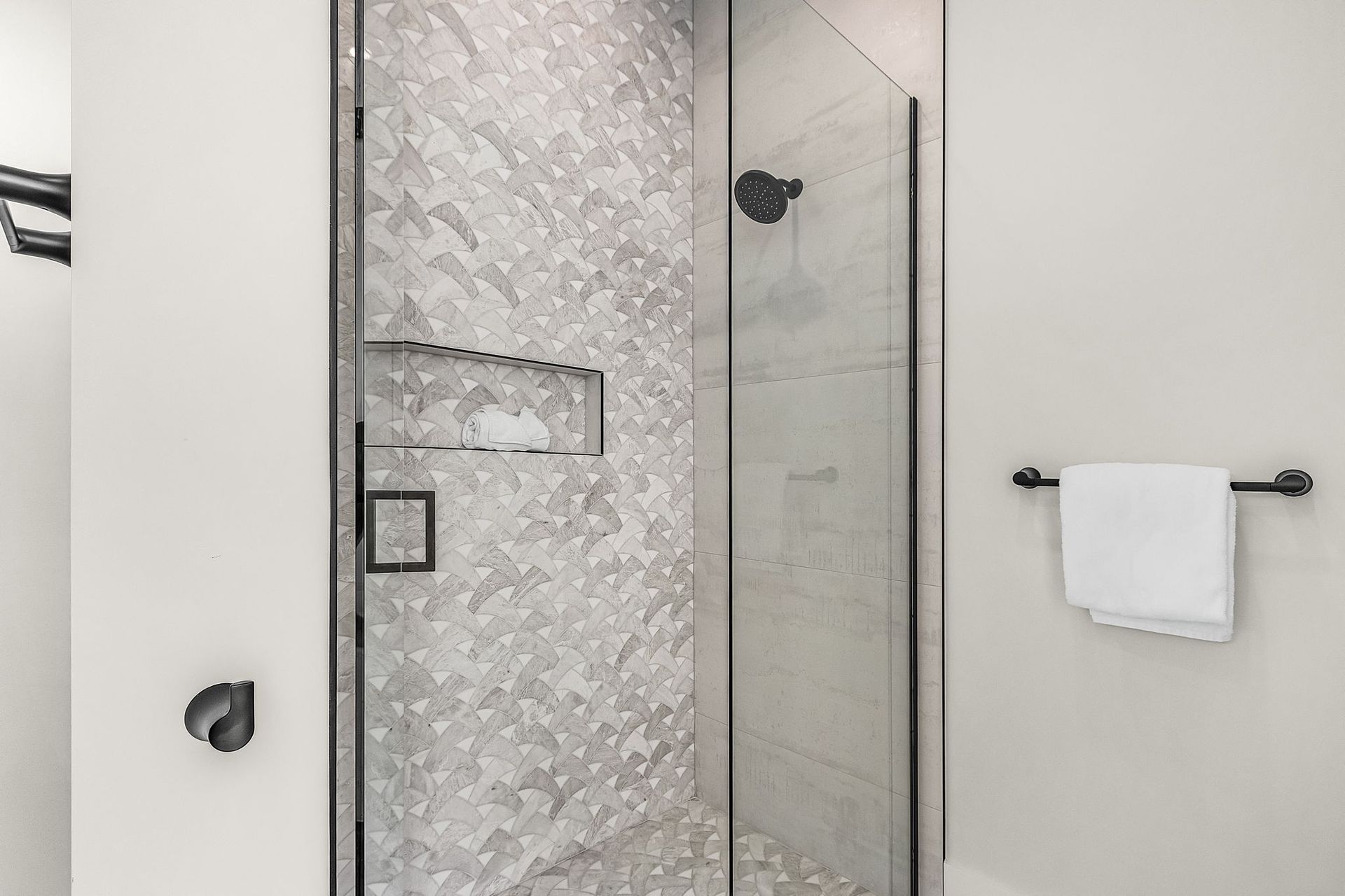 Bathroom with glass shower, gray and white tile, black fixtures, and a towel.